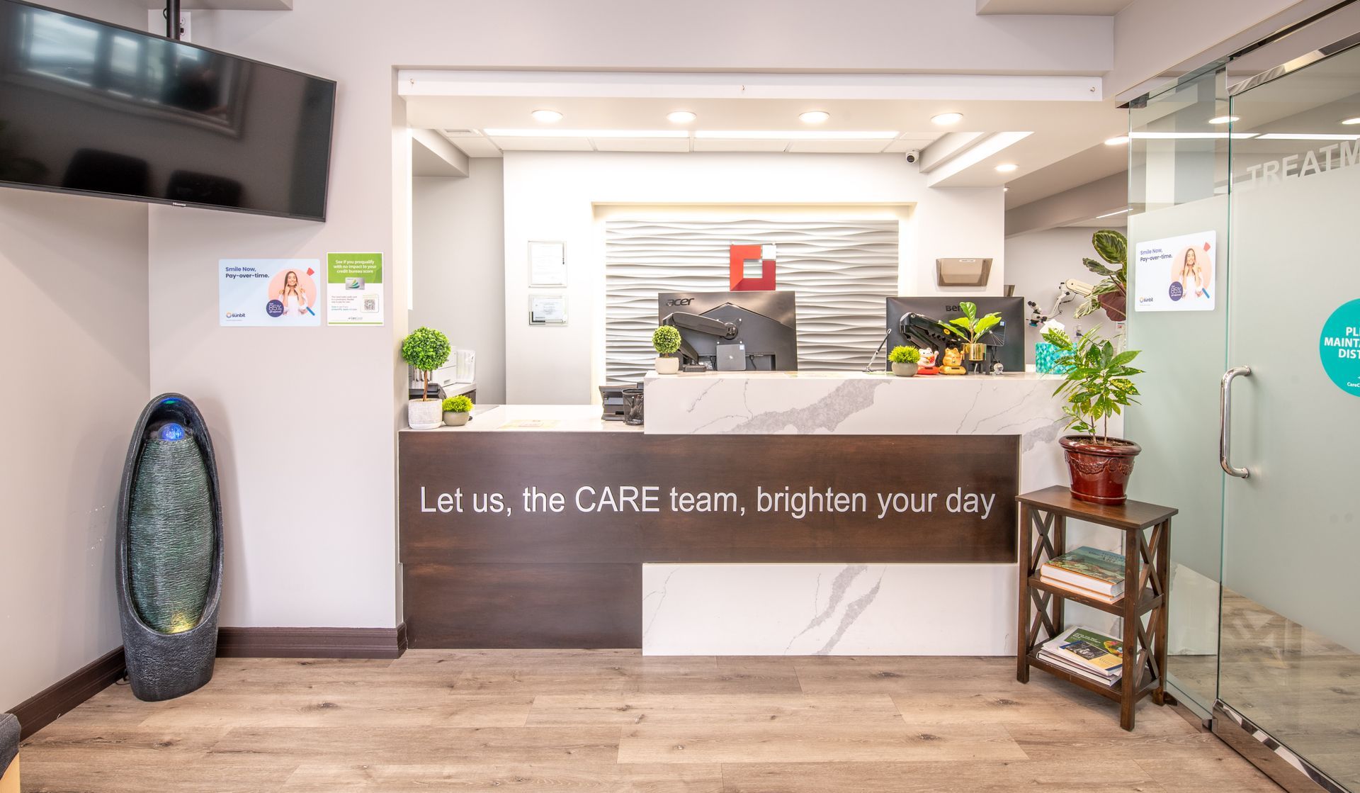 Reception area with desk, plants, and a sign that says “Let us, the CARE team, brighten your day”.