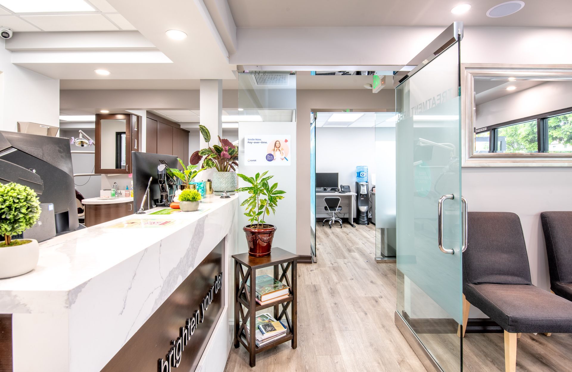 Reception area with a marble-topped desk, plants, and waiting chairs. A doorway leads to an office space.