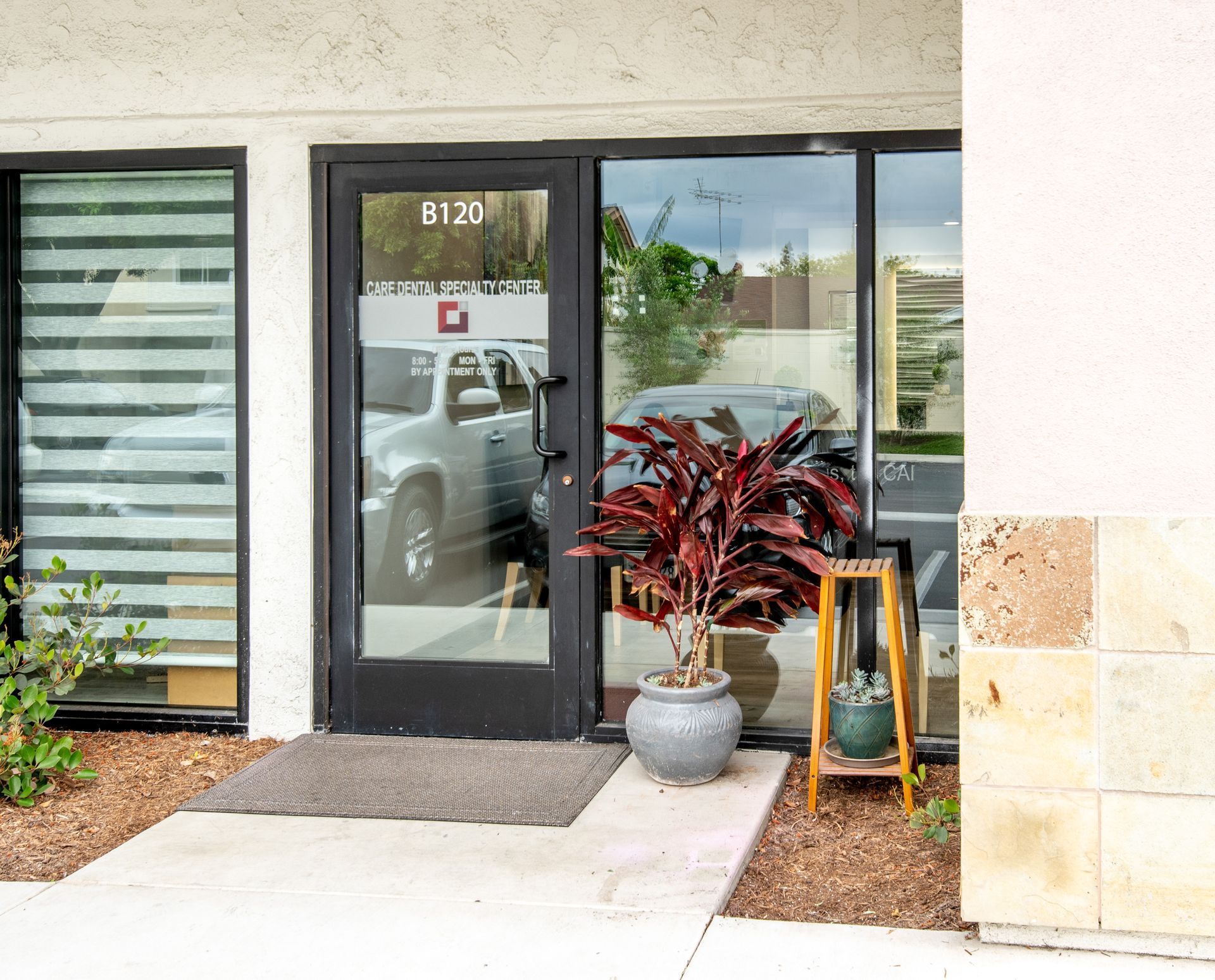 Entrance to a business with door, windows, and plants in pots. Building has light-colored stone facade.