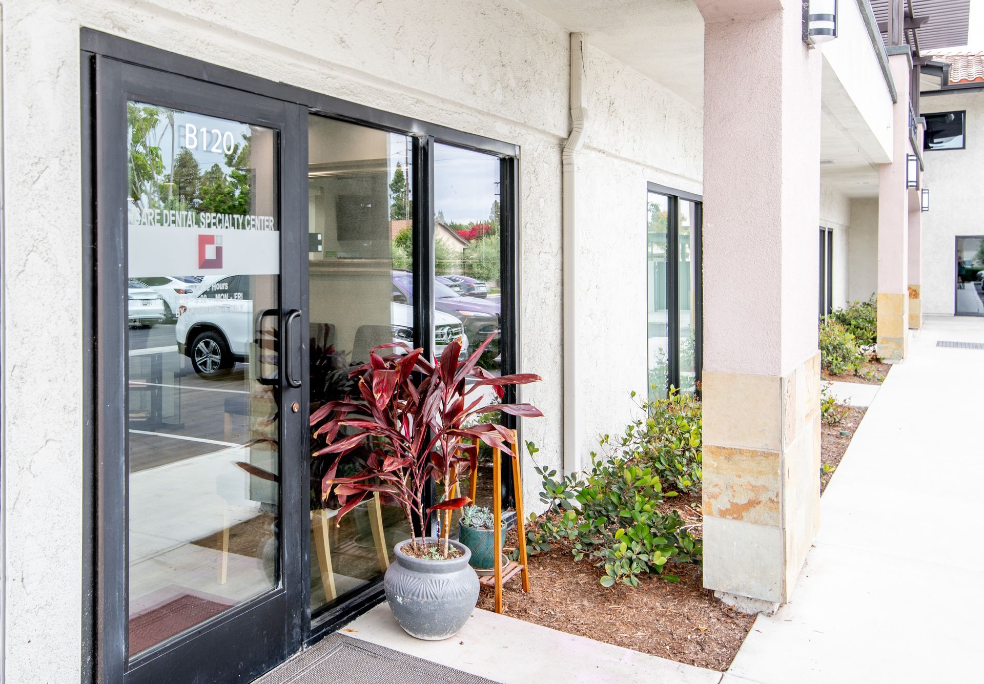 Exterior of an office with glass doors, a potted plant, and a pathway.