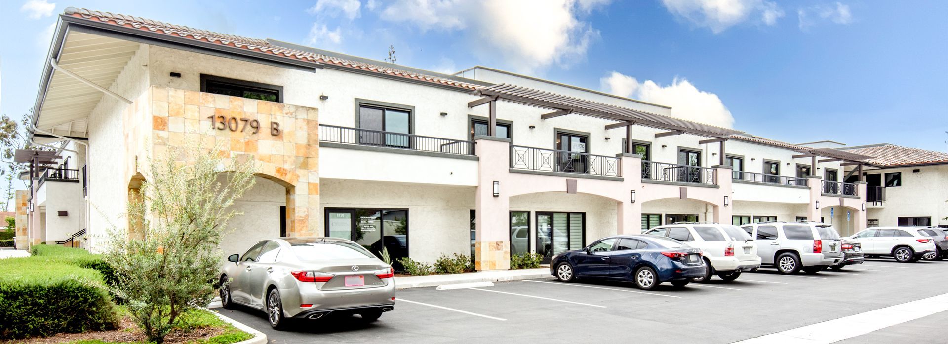 A two-story white building with black window frames, cars parked in front, and a clear blue sky.
