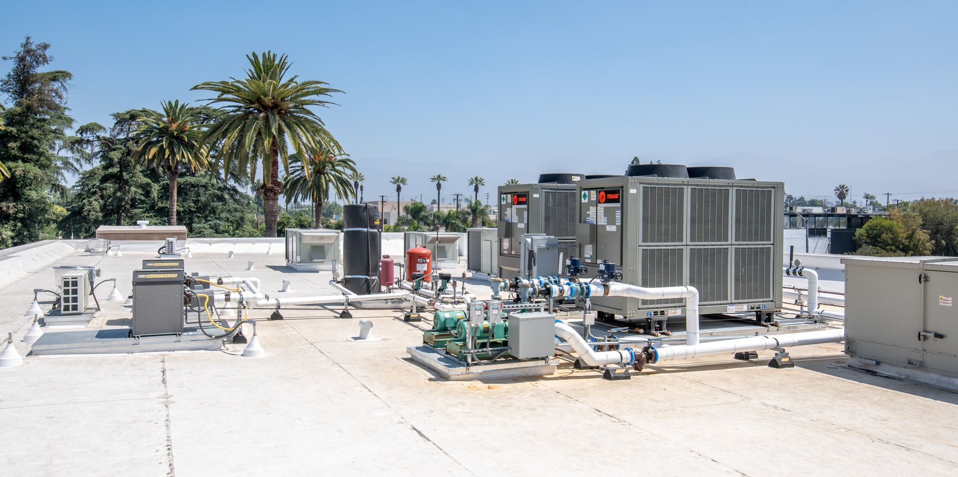 Rooftop equipment, including HVAC units, against a blue sky with palm trees in the background.