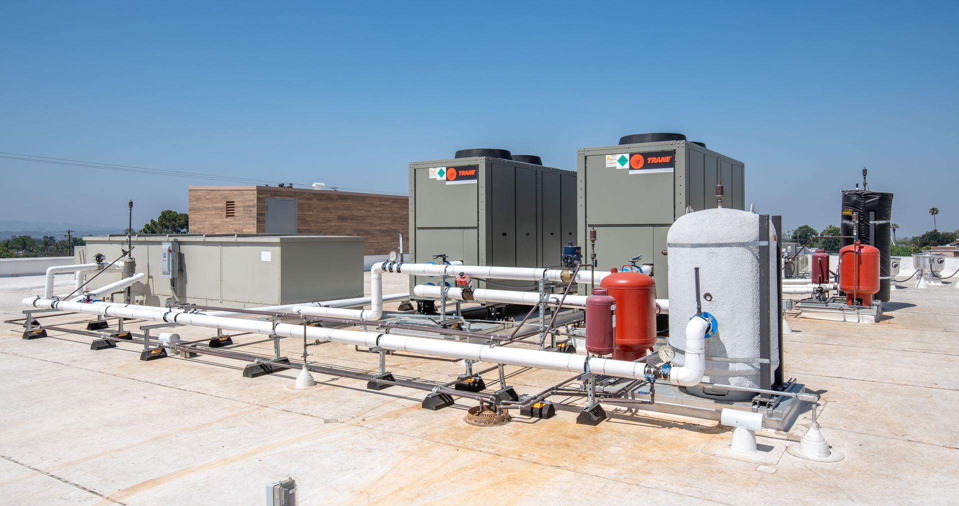Rooftop HVAC system with gray units, pipes, and red tanks against a blue sky.