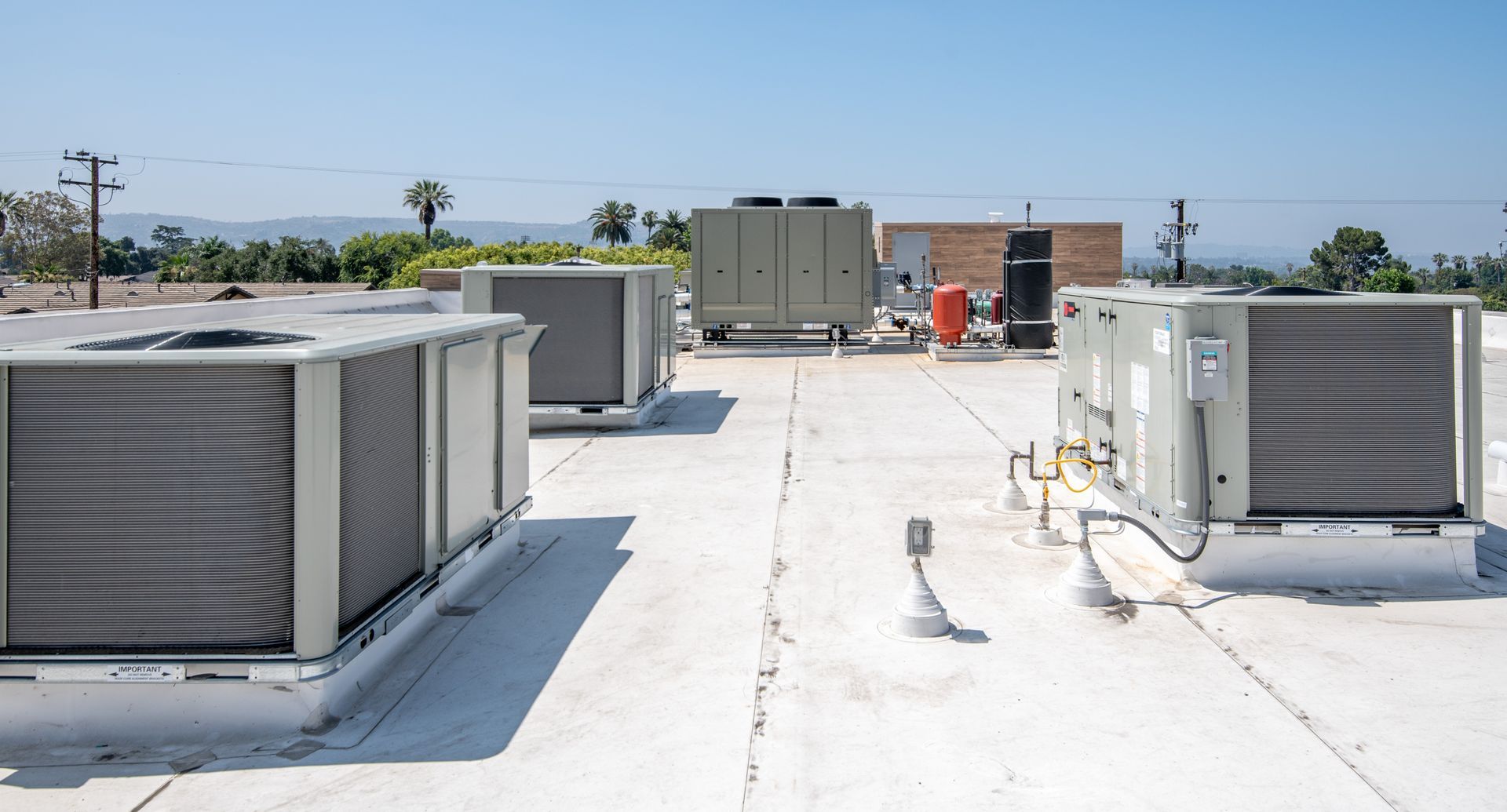 Rooftop with multiple large HVAC units on a white roof under a blue sky.