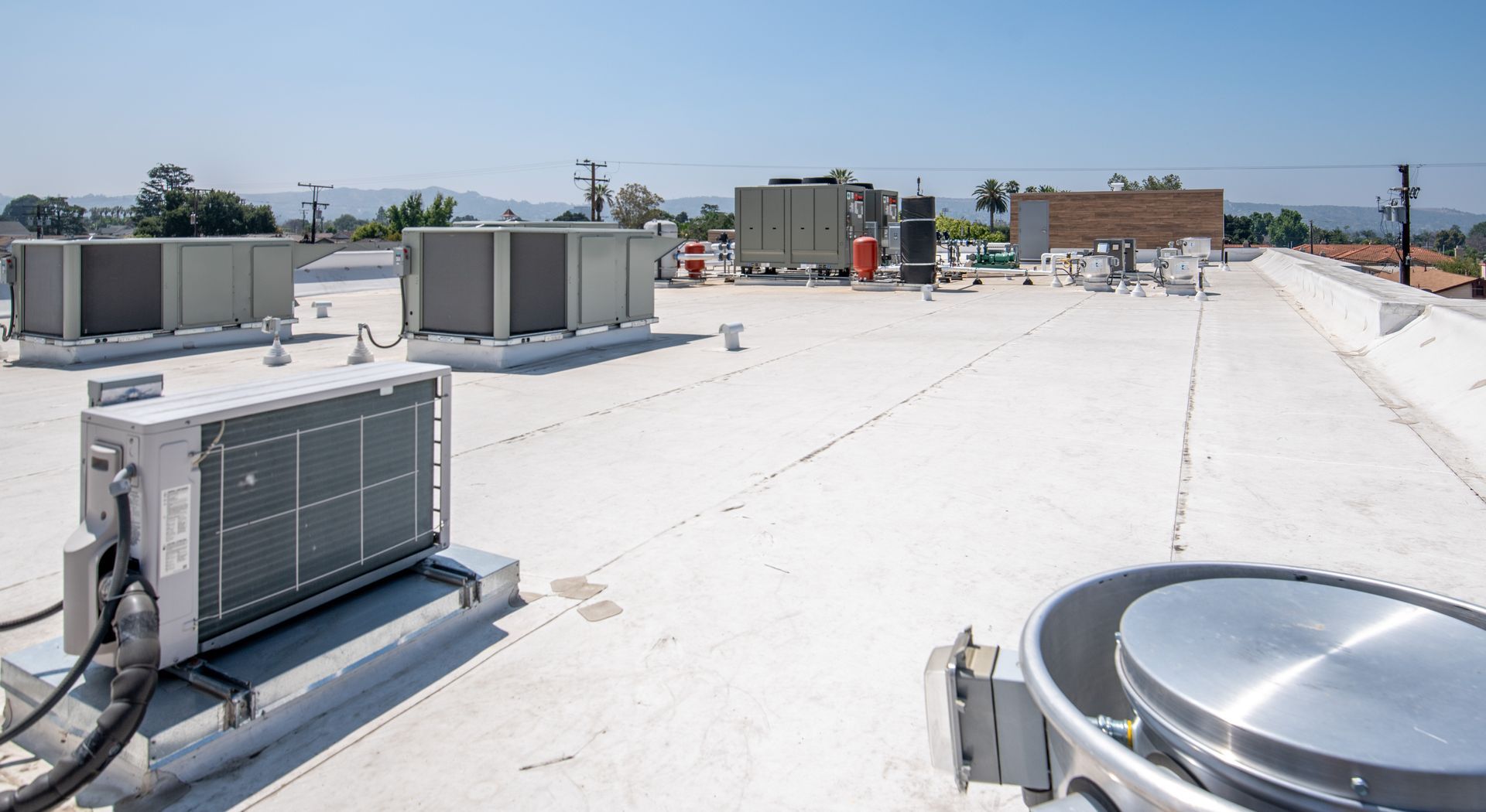 A flat roof with HVAC units, sunny day. White roof, gray units, distant hills.