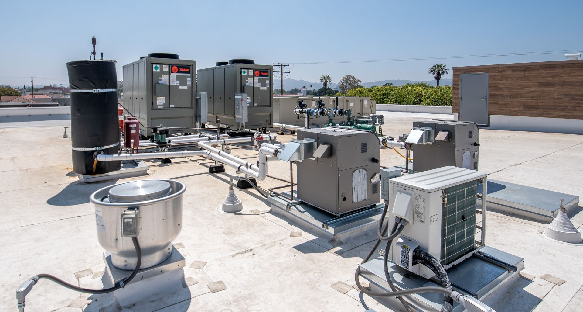 HVAC equipment on a flat rooftop, including air conditioning units, pipes, and a large cylindrical vent.