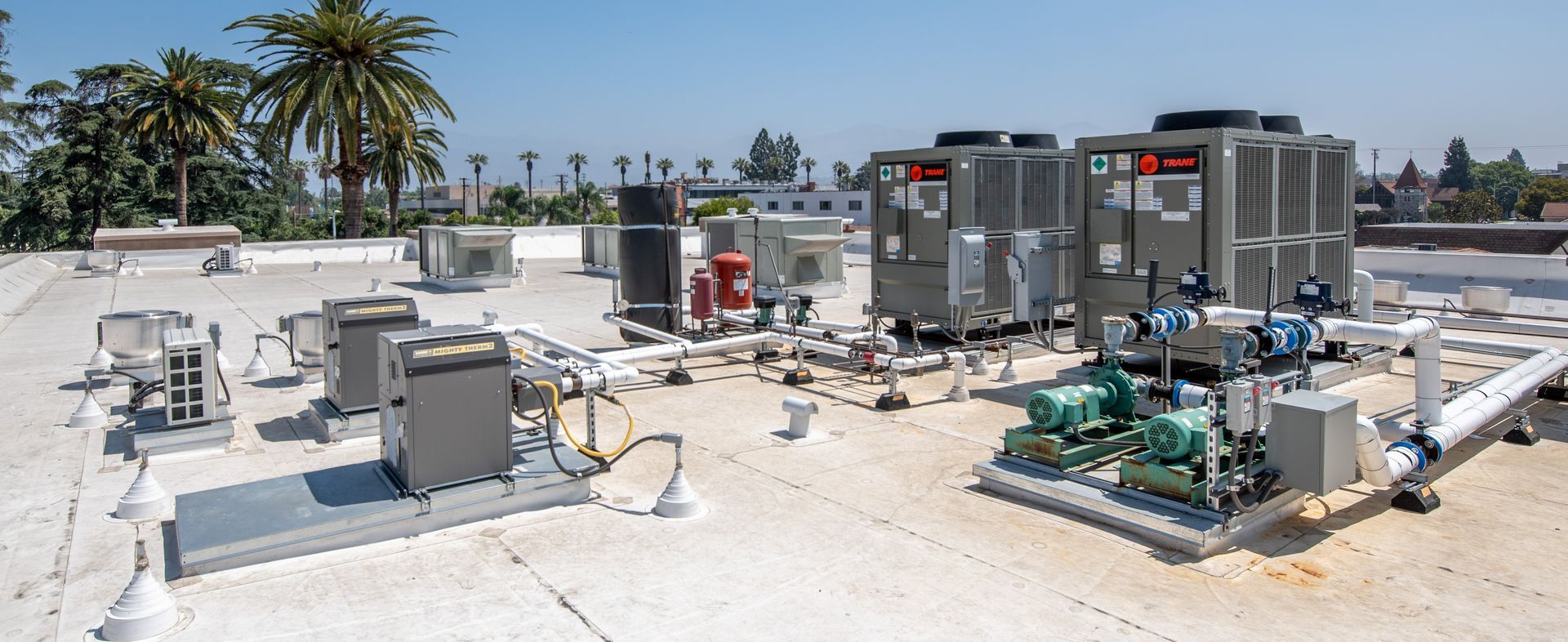 HVAC equipment on a flat roof on a sunny day.  Several gray air conditioning units and piping are visible.