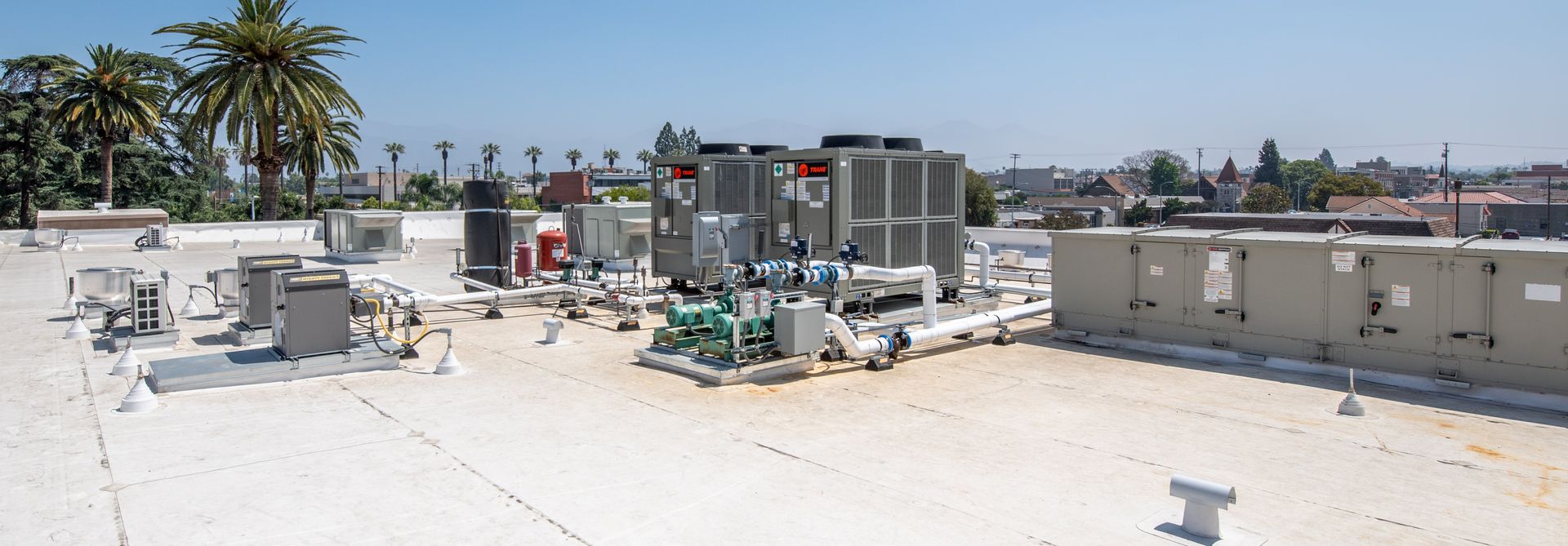 Rooftop with HVAC equipment on a bright, sunny day. City skyline in the background.