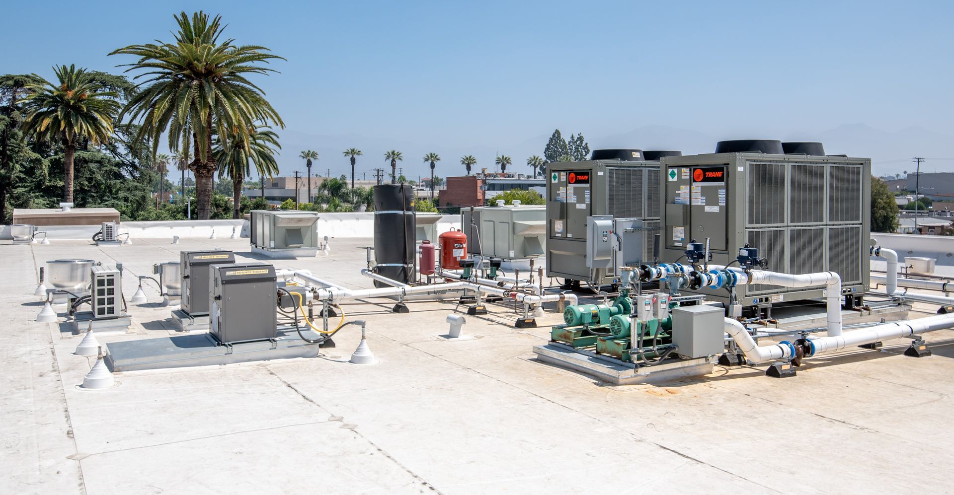 Rooftop with various air conditioning units, pipes, and machinery under a sunny sky.