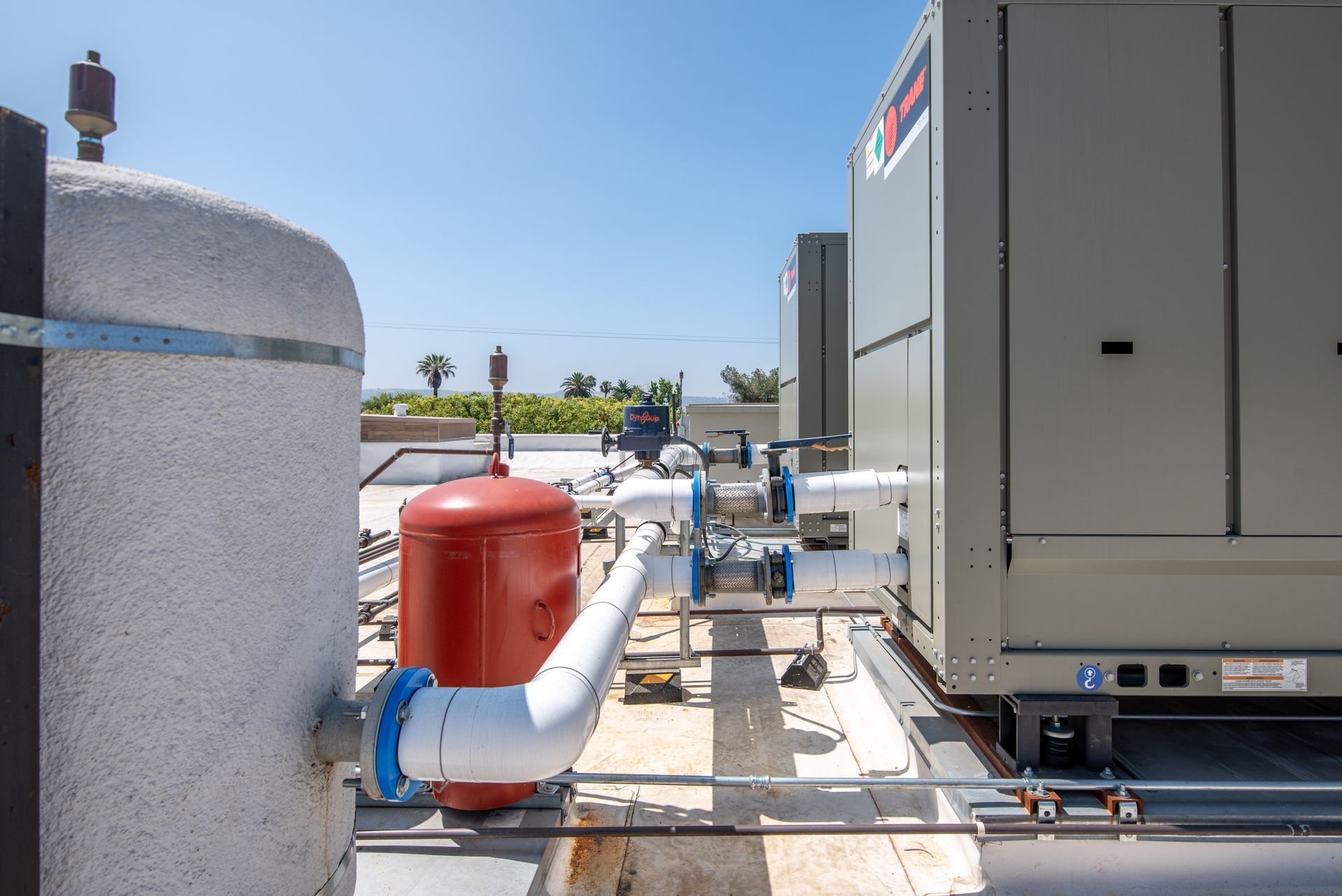 Rooftop HVAC equipment with white pipes, a red tank, and a gray unit, on a sunny day.