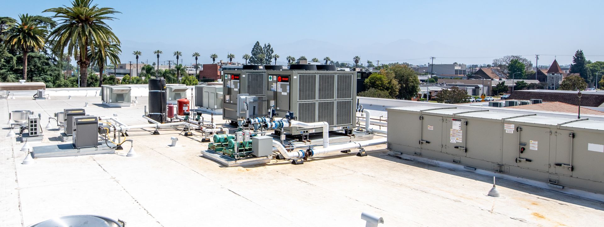 Rooftop with HVAC equipment under a blue sky, palm trees in background.