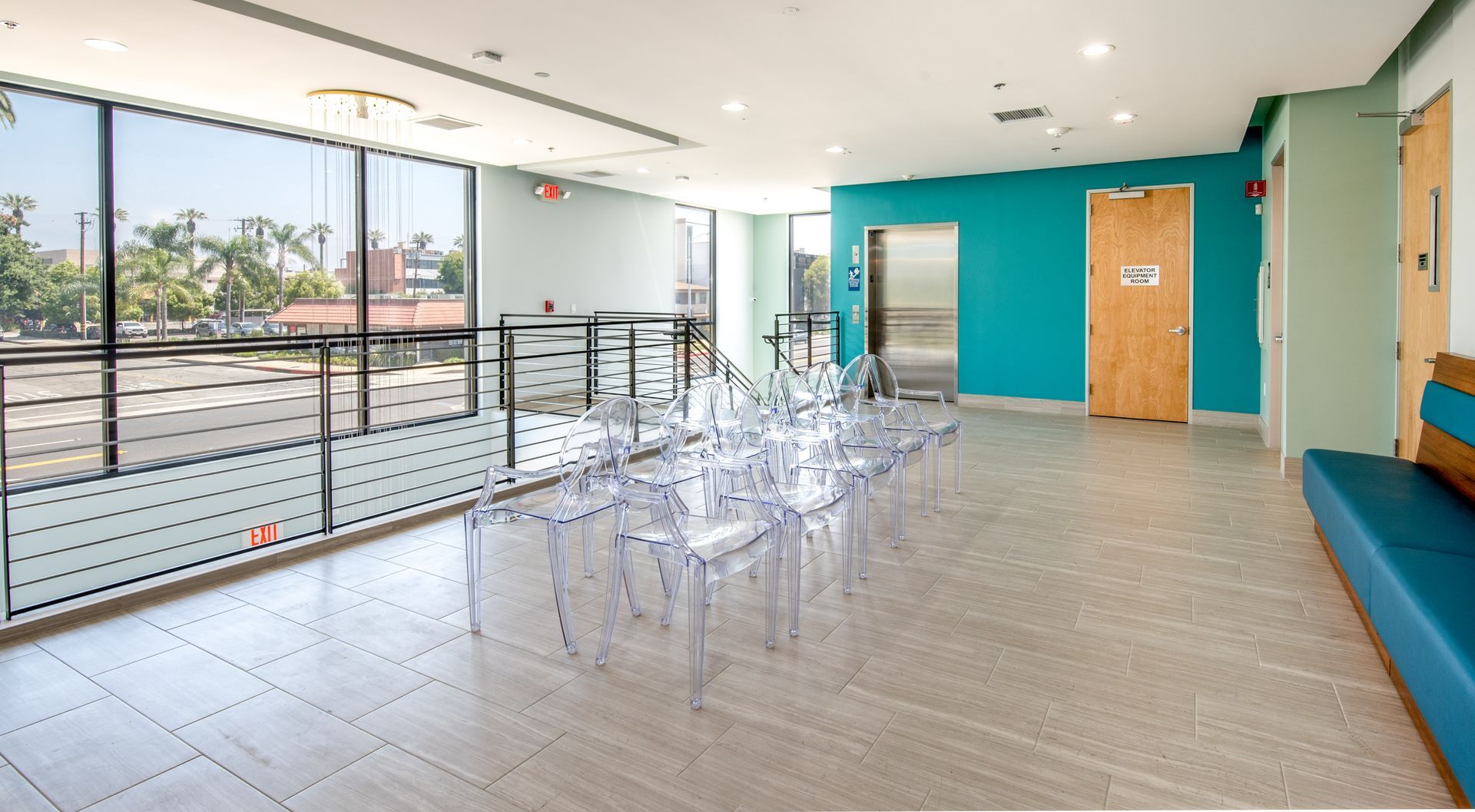 Bright waiting room with transparent chairs, blue walls, and large windows overlooking greenery.