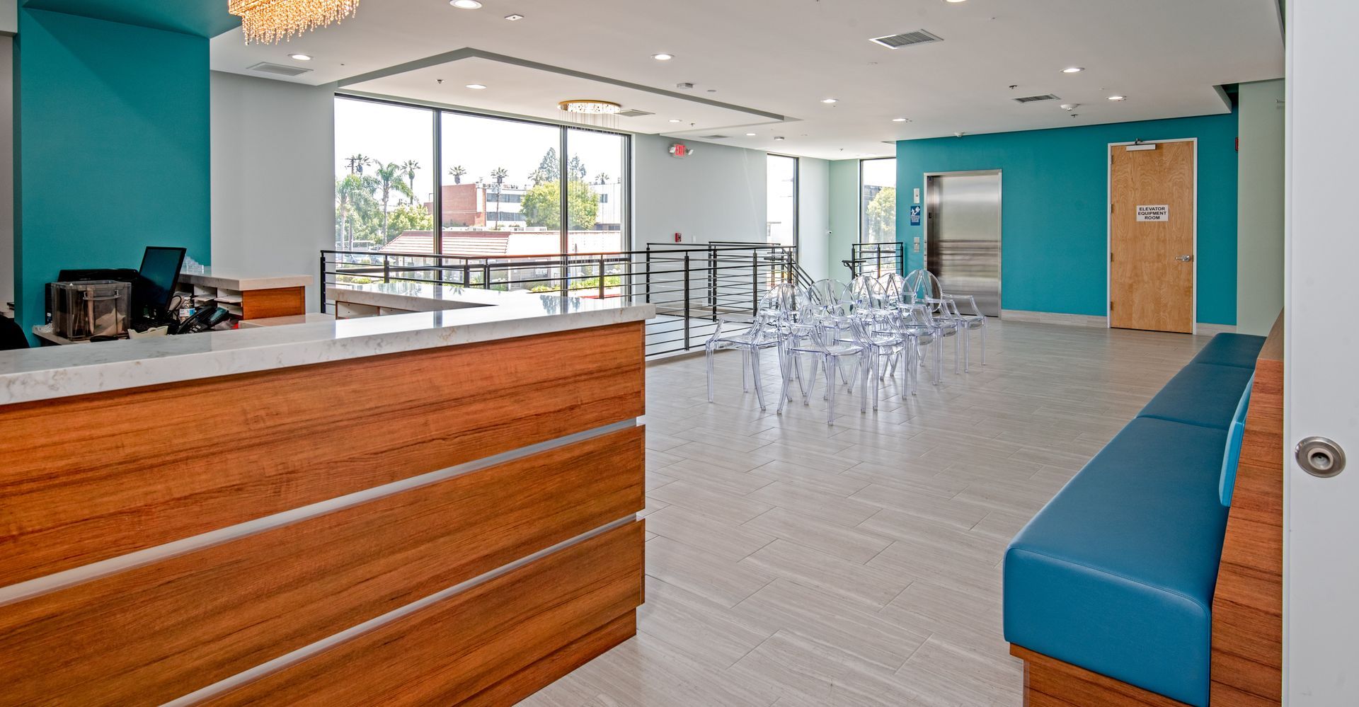 Reception area with wooden desk, teal walls, large windows, and blue bench.