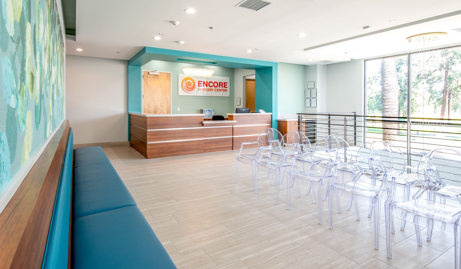Reception area with blue accents, wooden desk, clear chairs, and large windows.