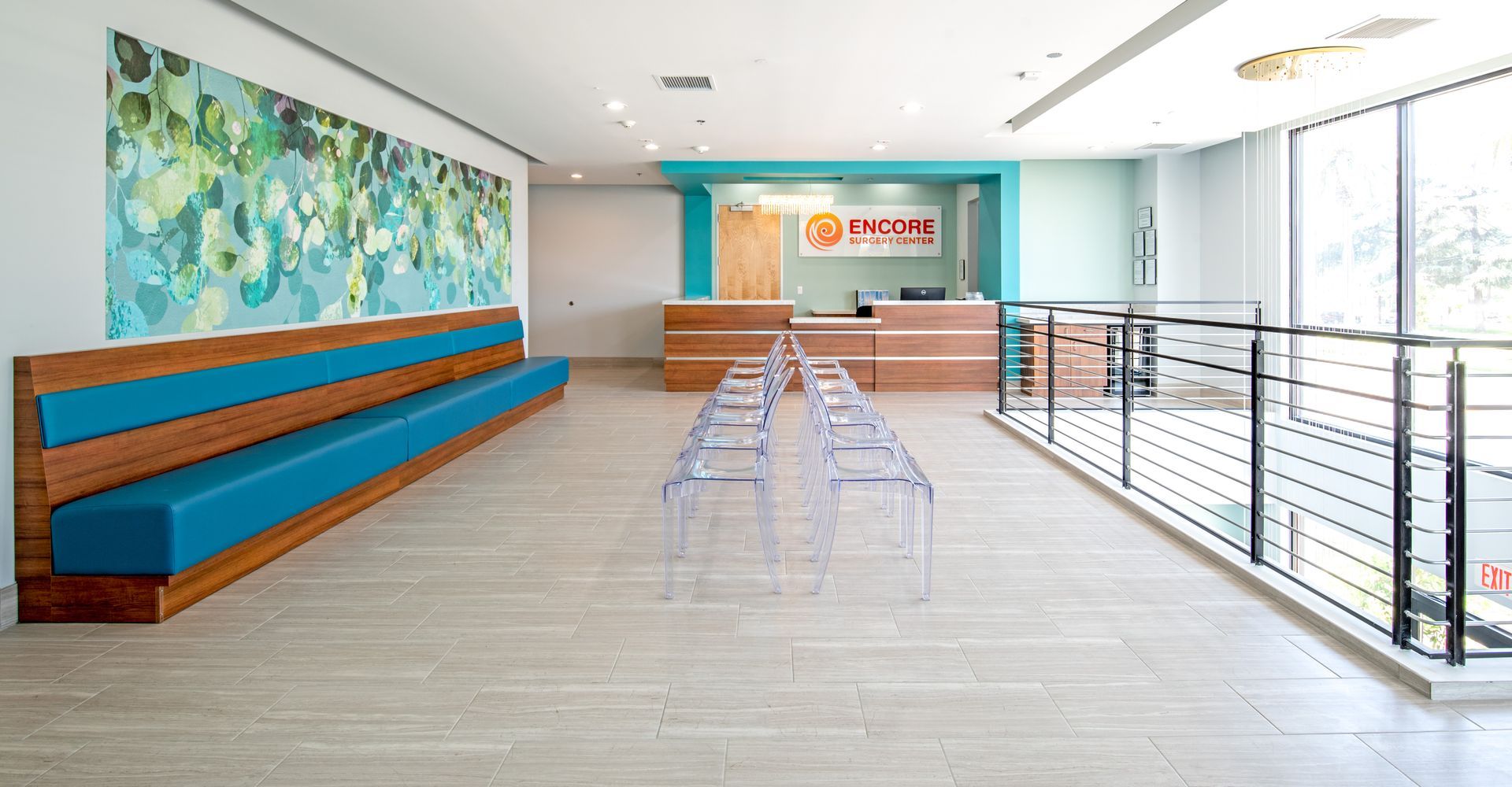 Waiting area of a clinic with a wooden bench, teal accents, reception desk, and clear chairs.