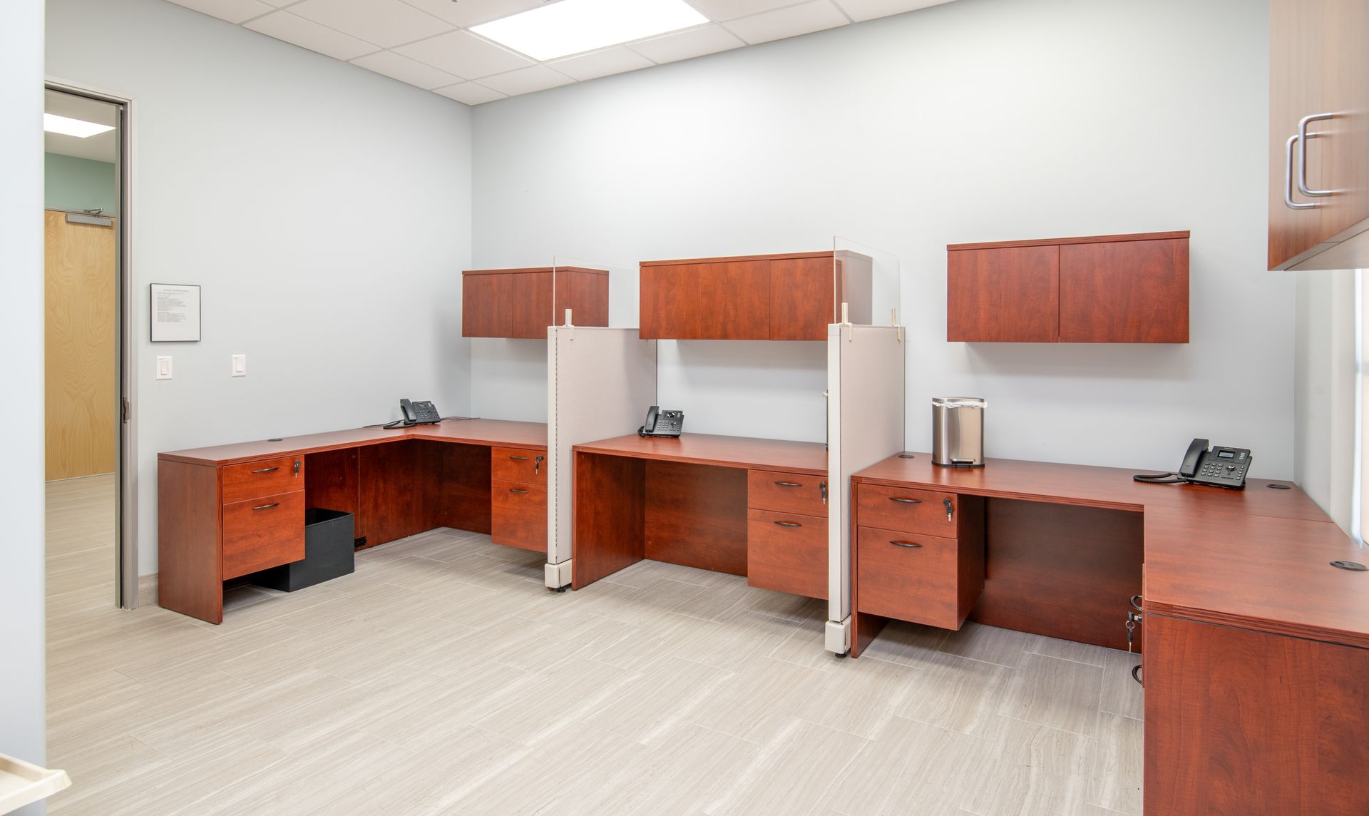 Office space with three wood desks, overhead cabinets, and a door on the left.