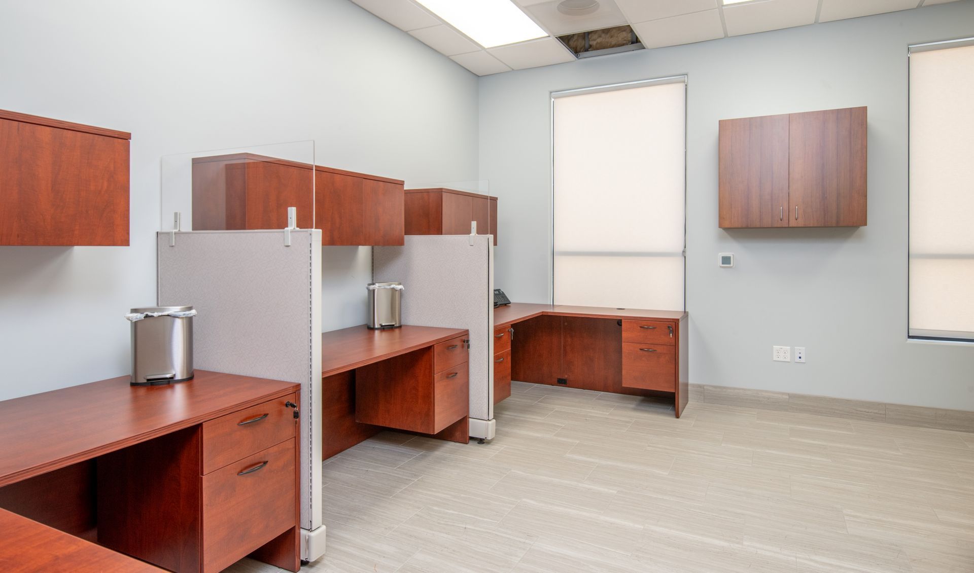 Empty office cubicles with brown desks and cabinets, light gray walls, and carpet.
