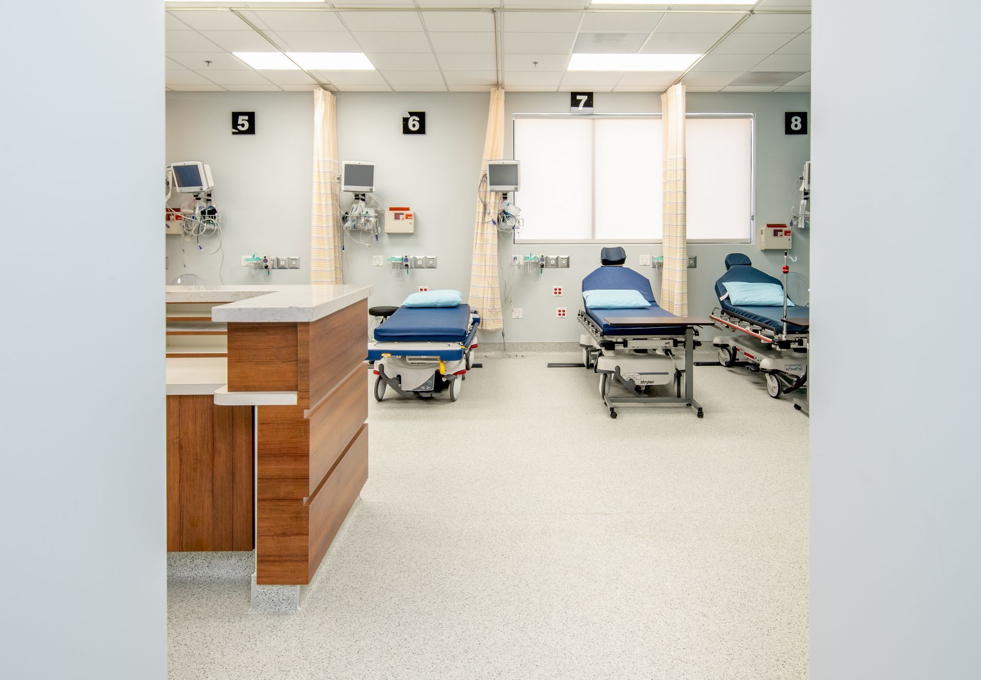 An empty hospital room with three beds, medical equipment, and a wooden desk.