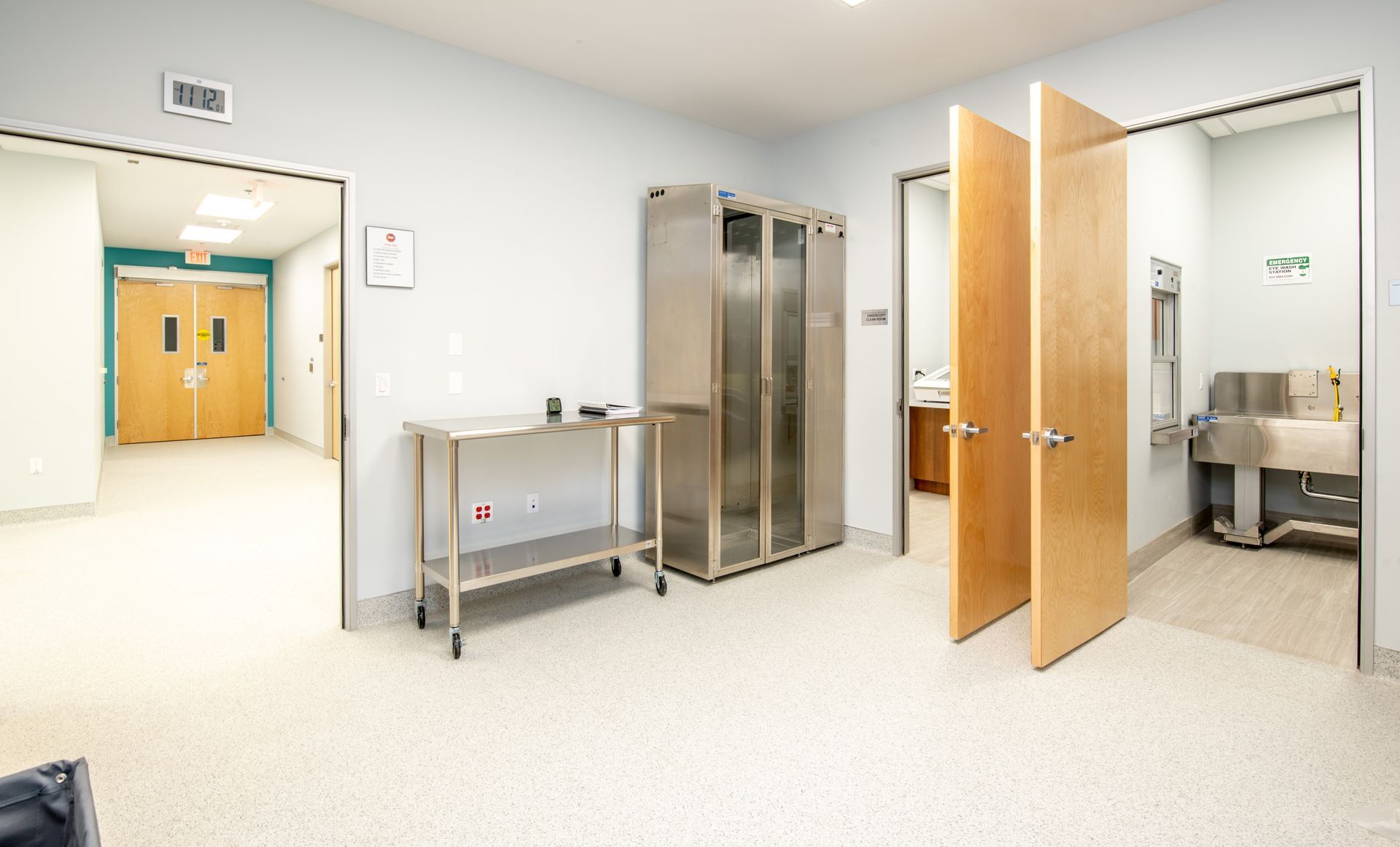 A hospital room with stainless steel cabinets, table, and two open doors.