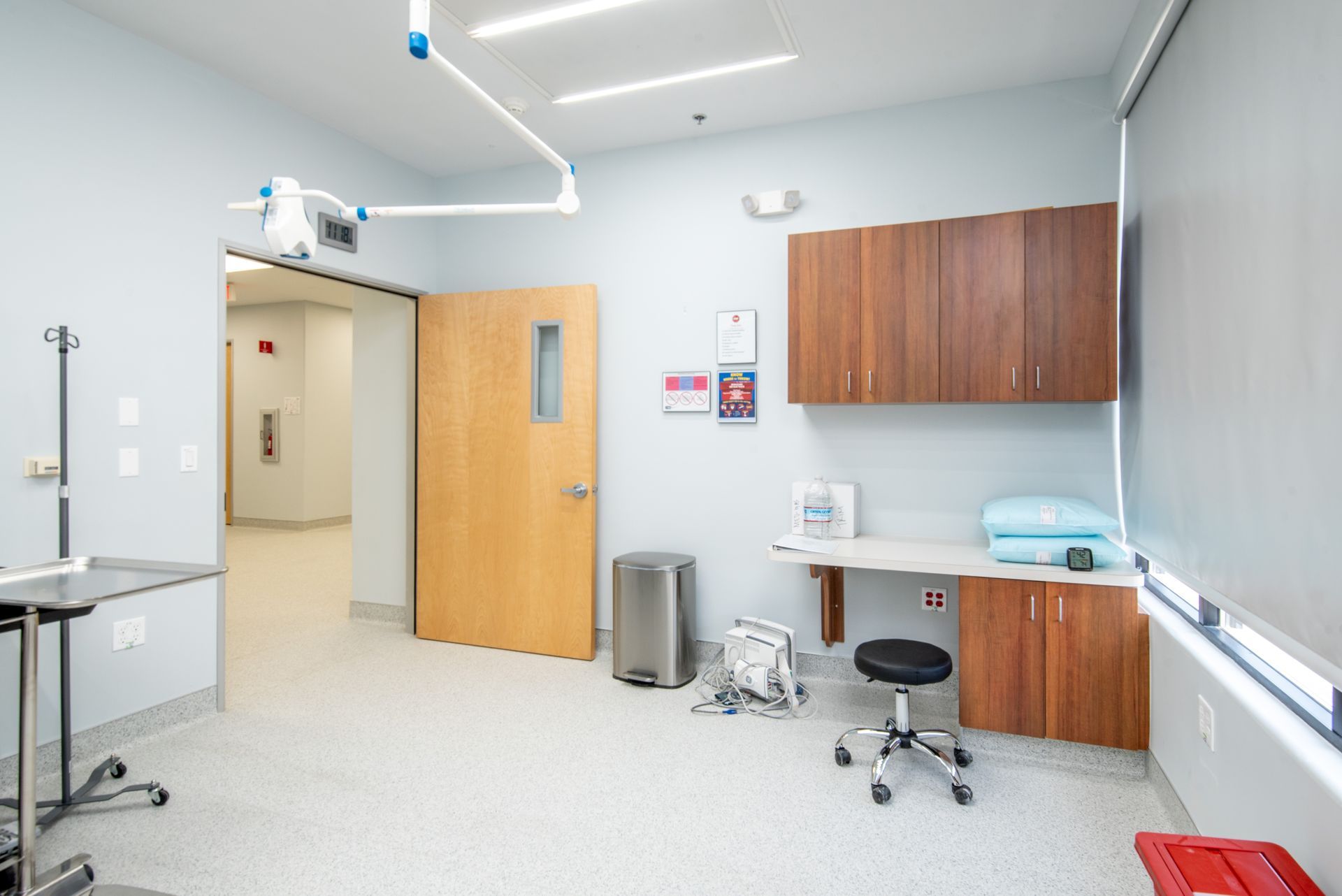 Examination room with cabinets, desk, surgical light, door, and window.