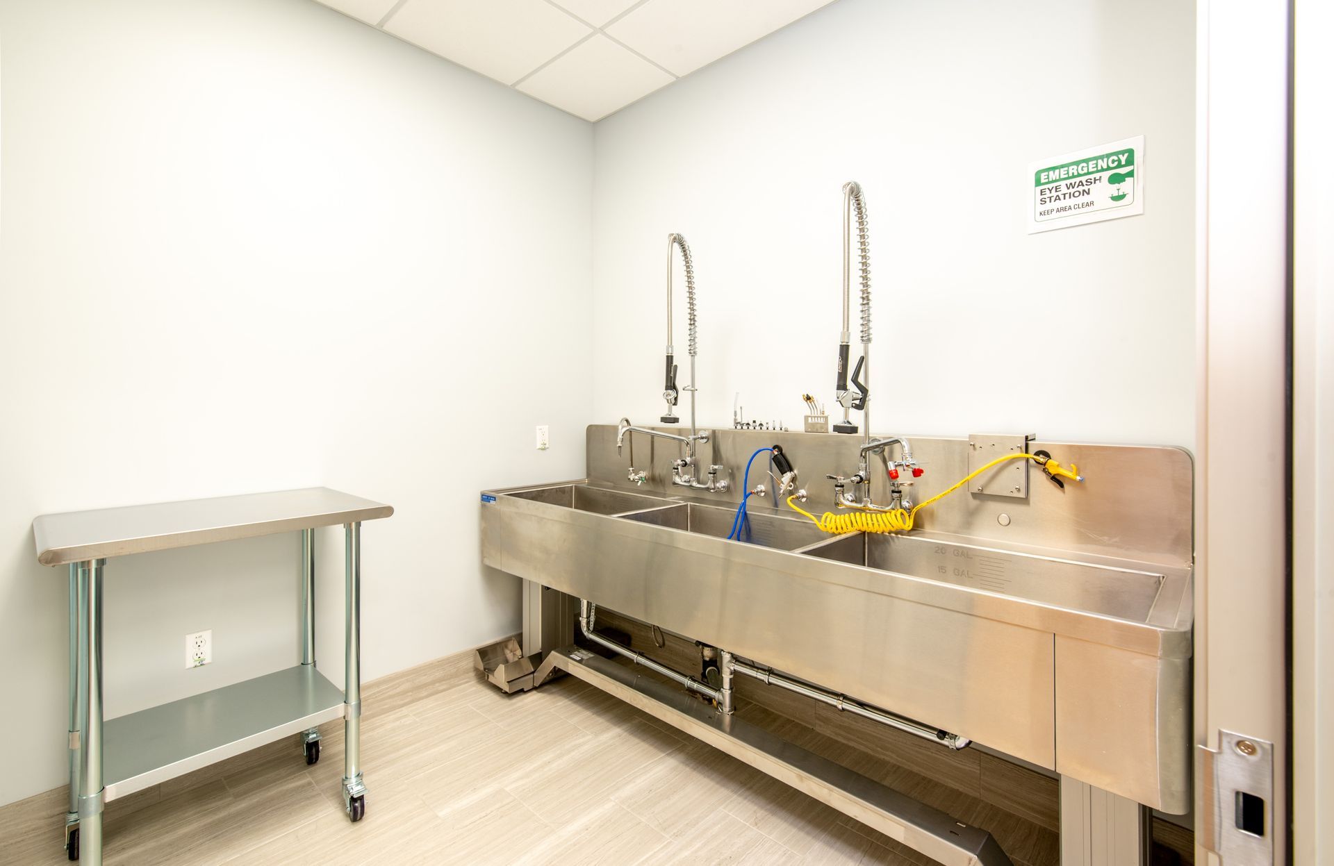 A laboratory sink with multiple faucets, a side table, and an emergency eye wash station.