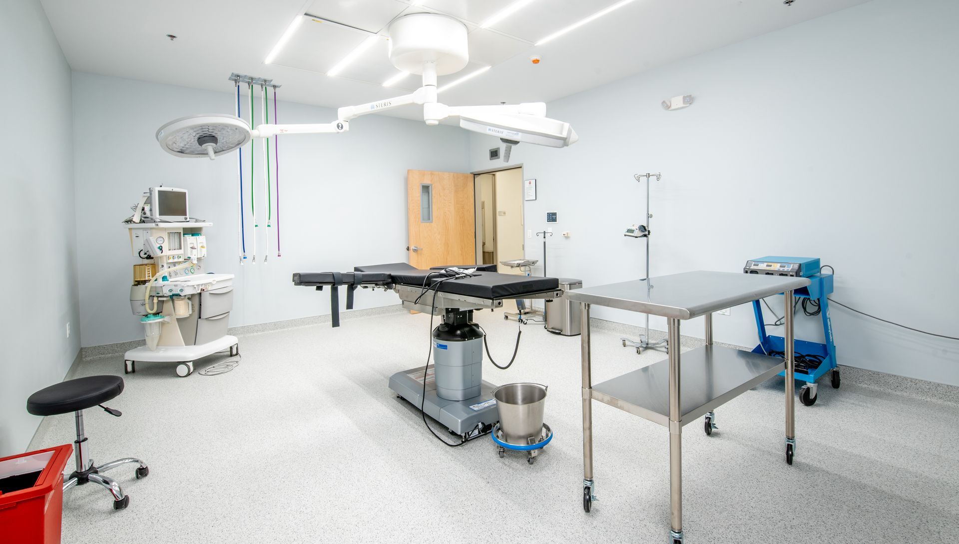 An empty, bright operating room with a table, instruments, and equipment.