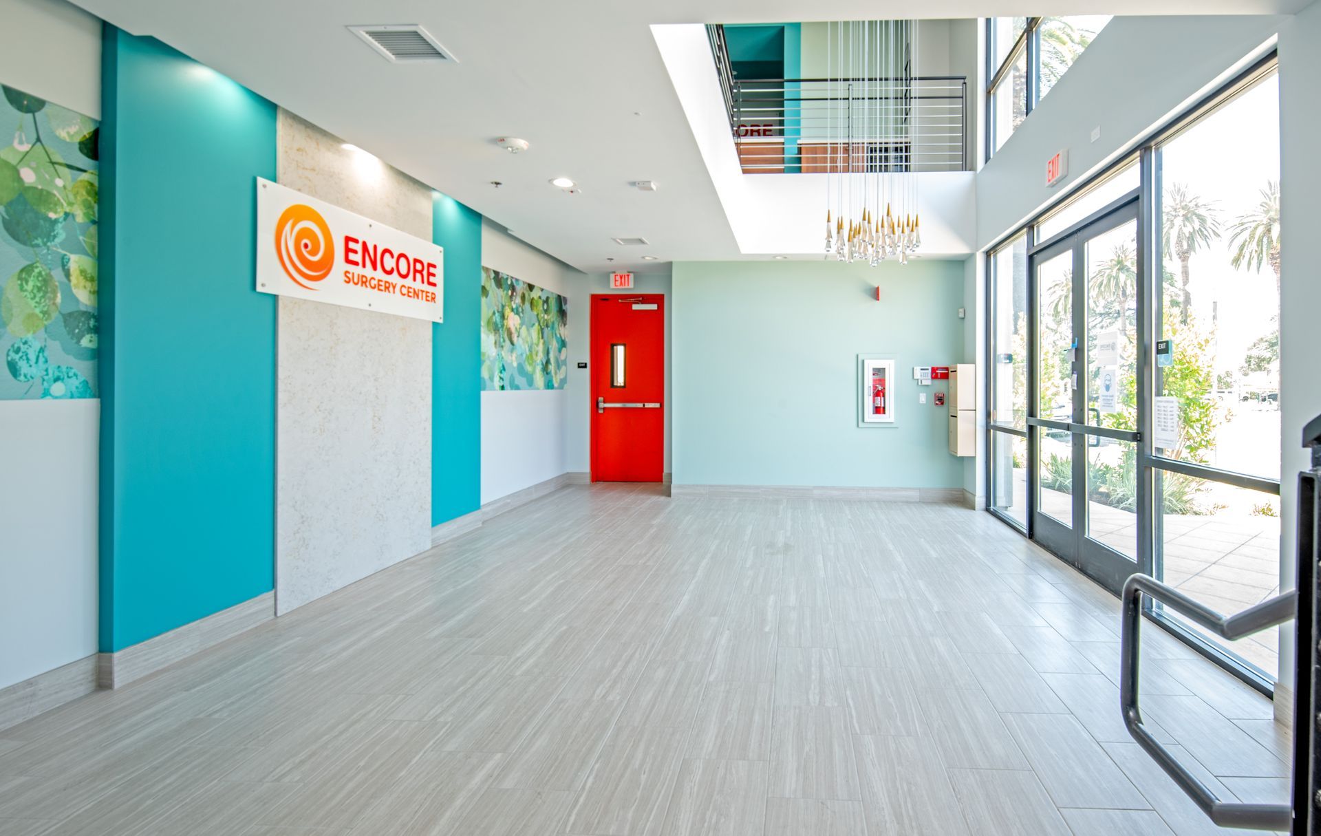Hallway with teal and white walls, red door, and large windows; 
