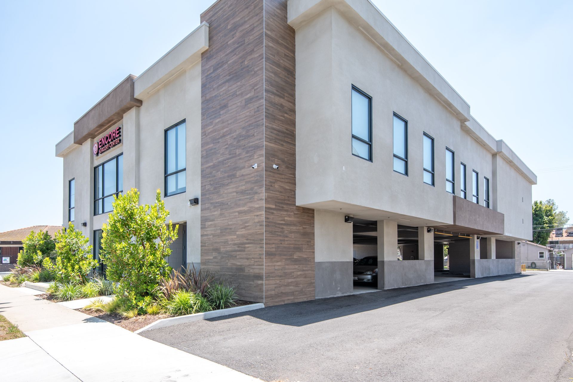 Modern two-story beige building with brown brick accents, windows, and a parking area.