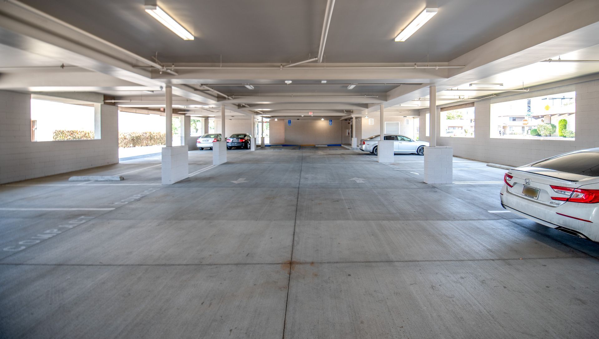 Empty indoor parking garage with concrete floor and pillars; cars parked on both sides.