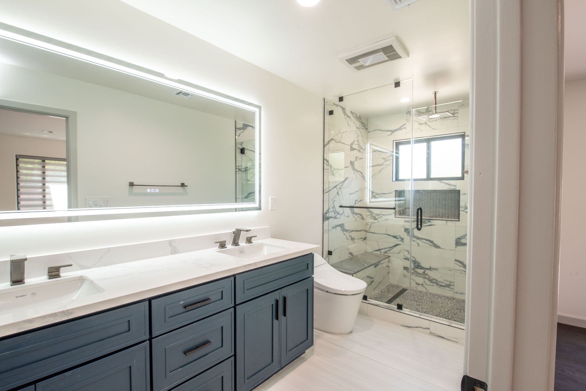 Modern blue-cabinet bathroom with large mirror, marble shower, and white toilet.