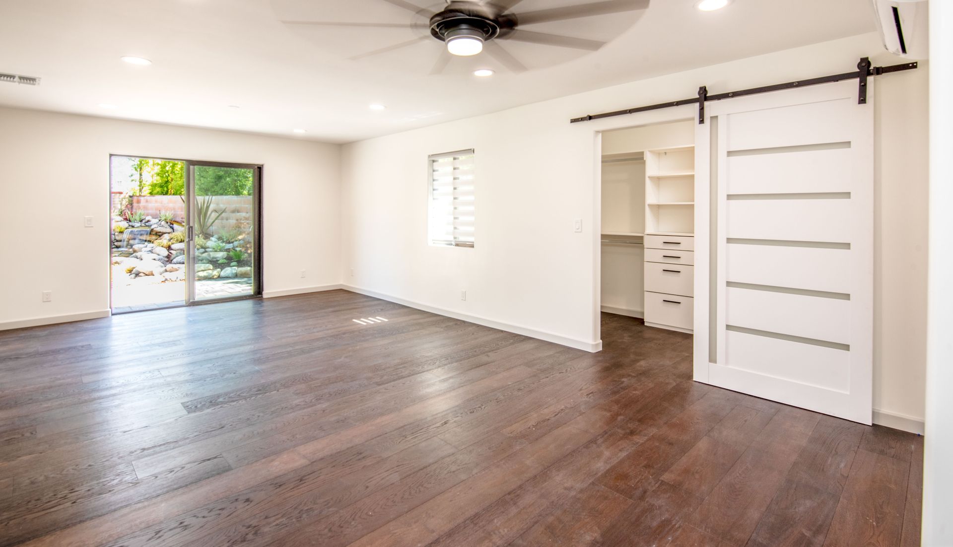 Spacious room with dark wood floors, sliding door to a yard, and a white barn door leading to a closet.