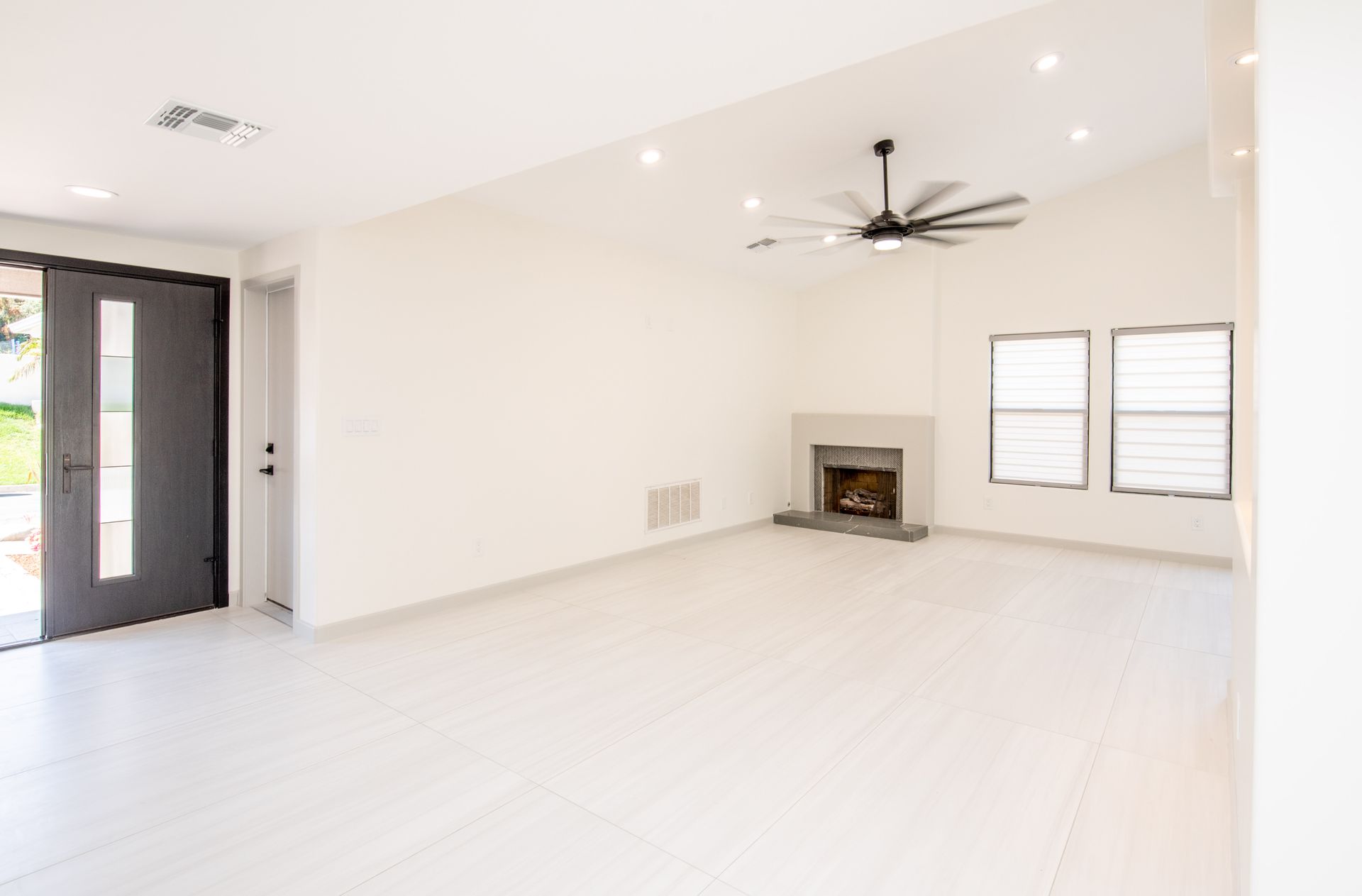 Empty, bright living room with white floors, fireplace, and open black front door.