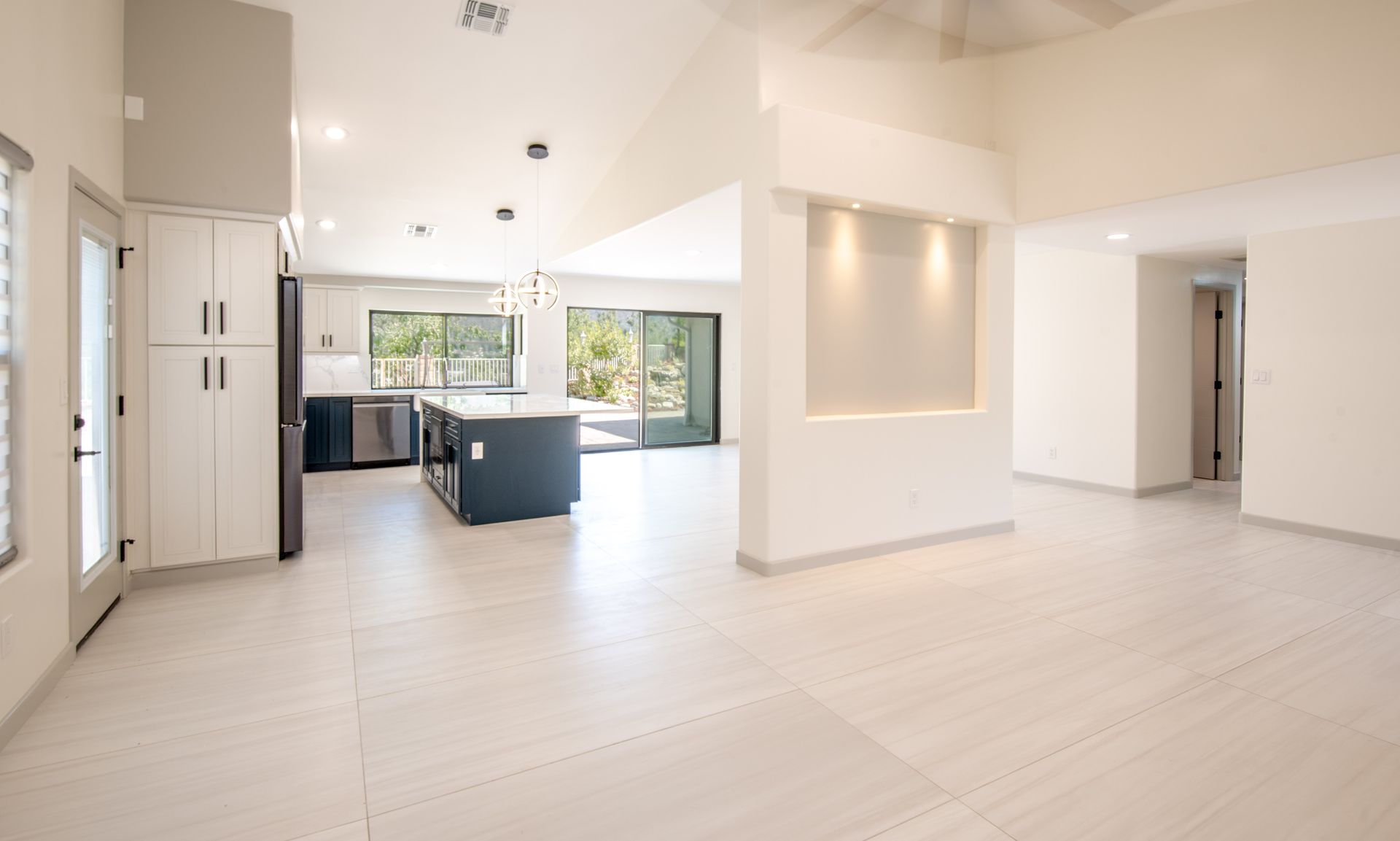 Bright interior of a modern home with open kitchen and living spaces, featuring white walls and a dark blue island.
