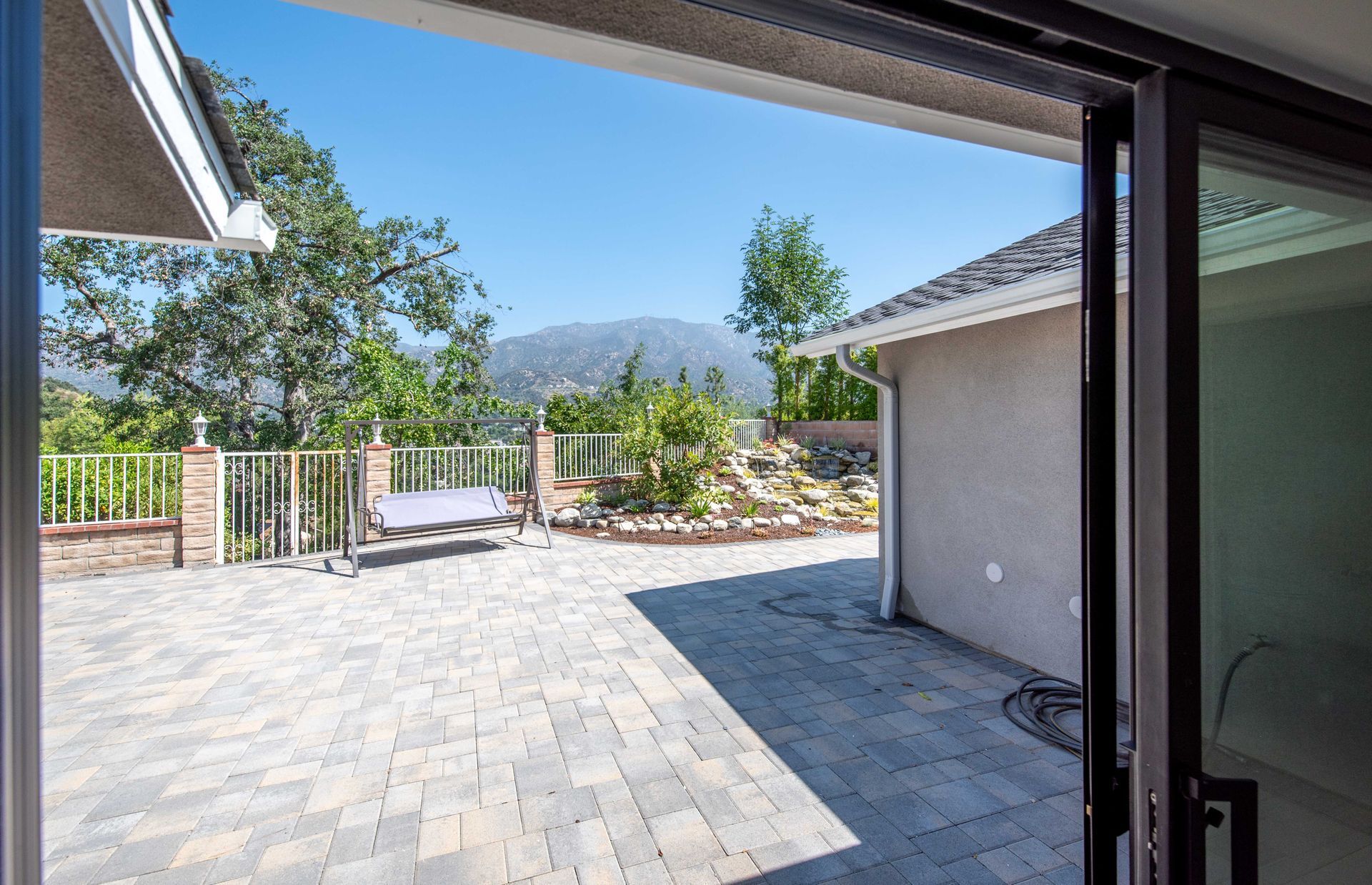 Patio view: brick patio, mountains, trees, and a swing visible through an open sliding door on a sunny day.