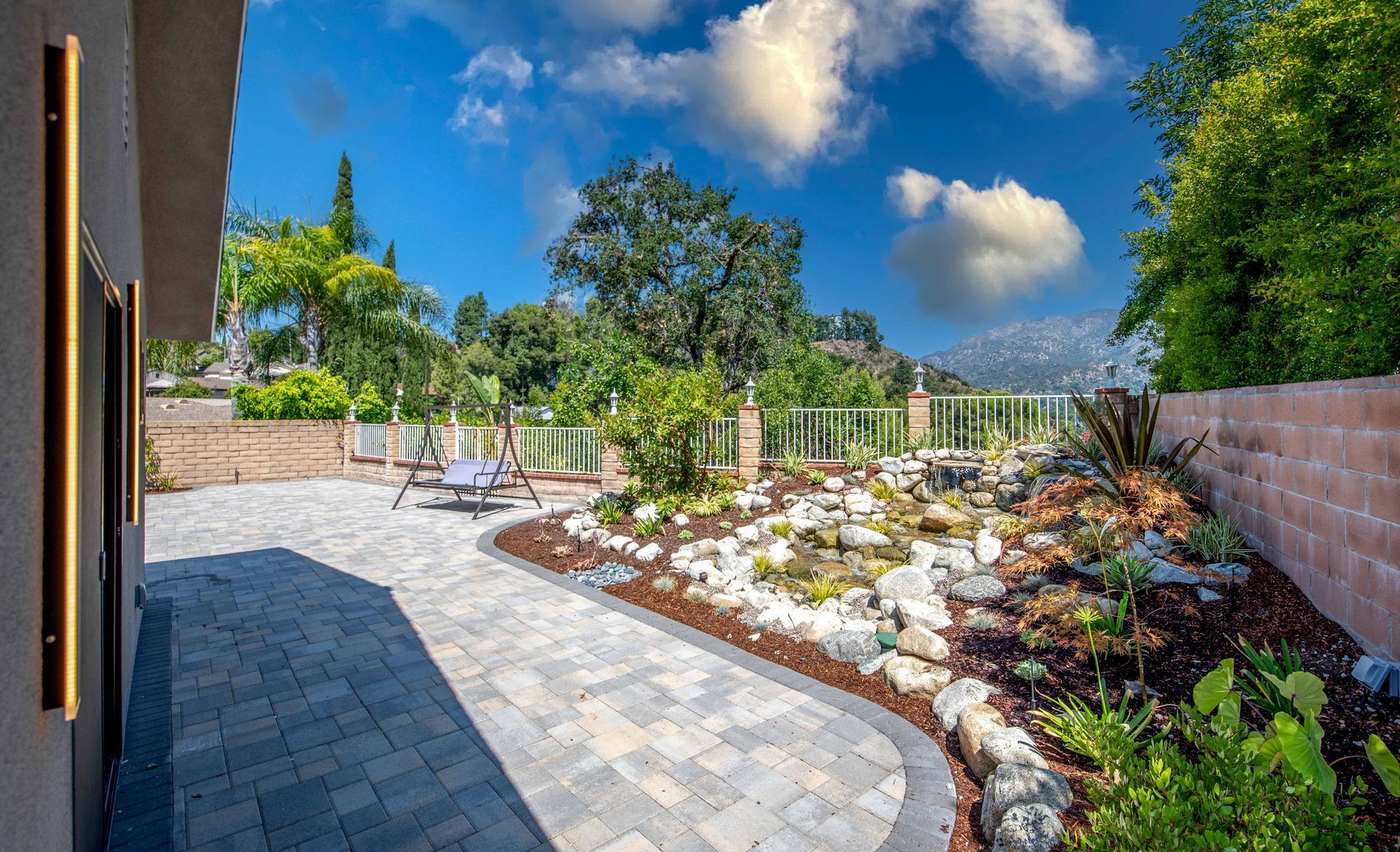 Patio with patterned pavers leads to a rock garden and landscaped area, under a blue sky.