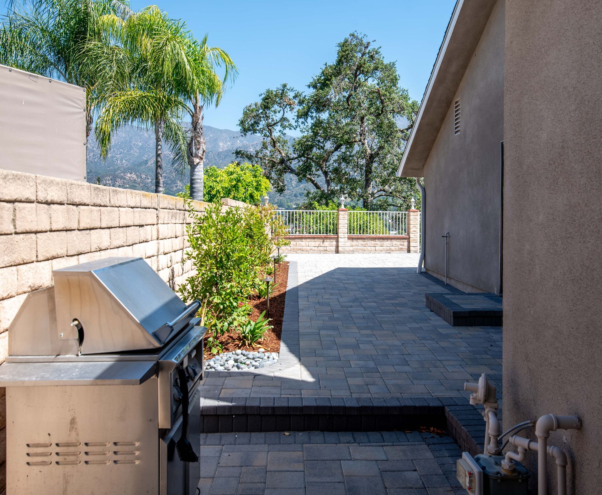 Backyard patio with grill, brick wall, plants, and mountain view.