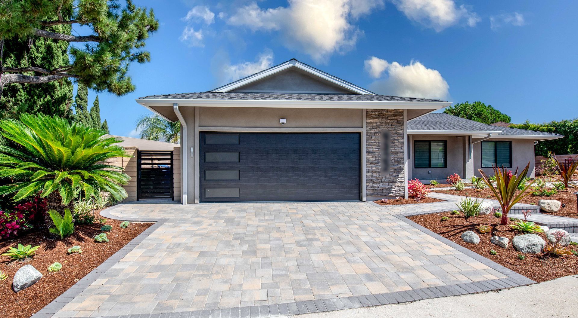 Modern home with gray garage door, stone accents, and landscaped yard with a blue sky.