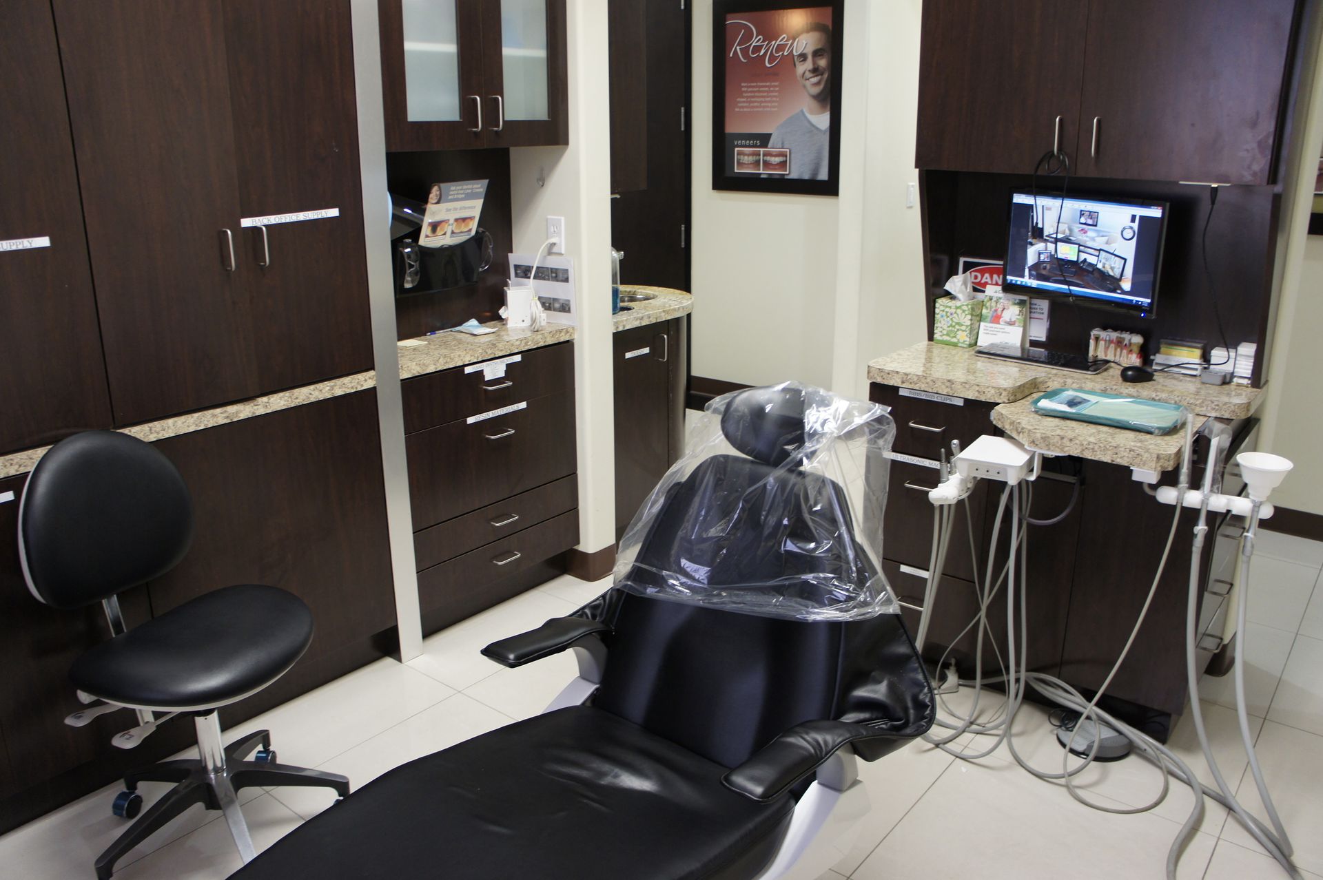 Dental office exam room, black dental chair, dark cabinets, computer screen.