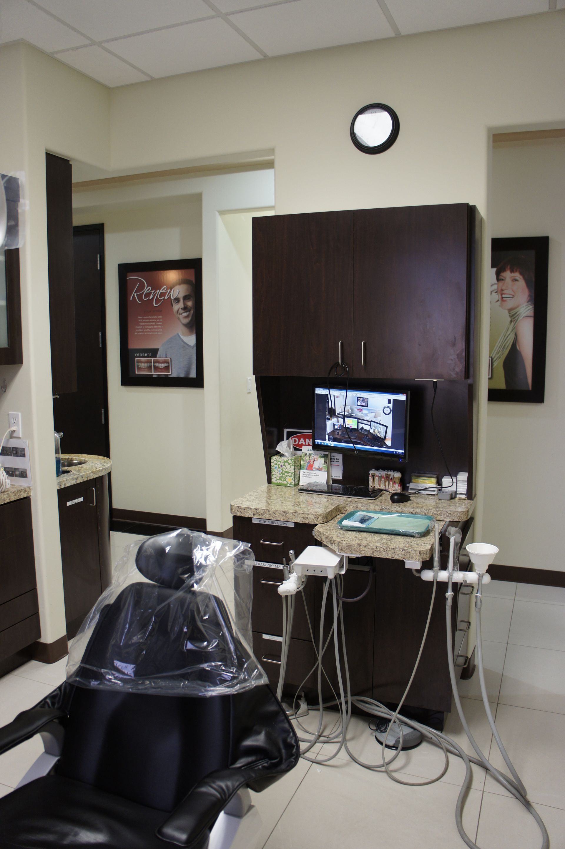 Dental operatory with black chair, dark wood cabinets, monitor, dental tools.