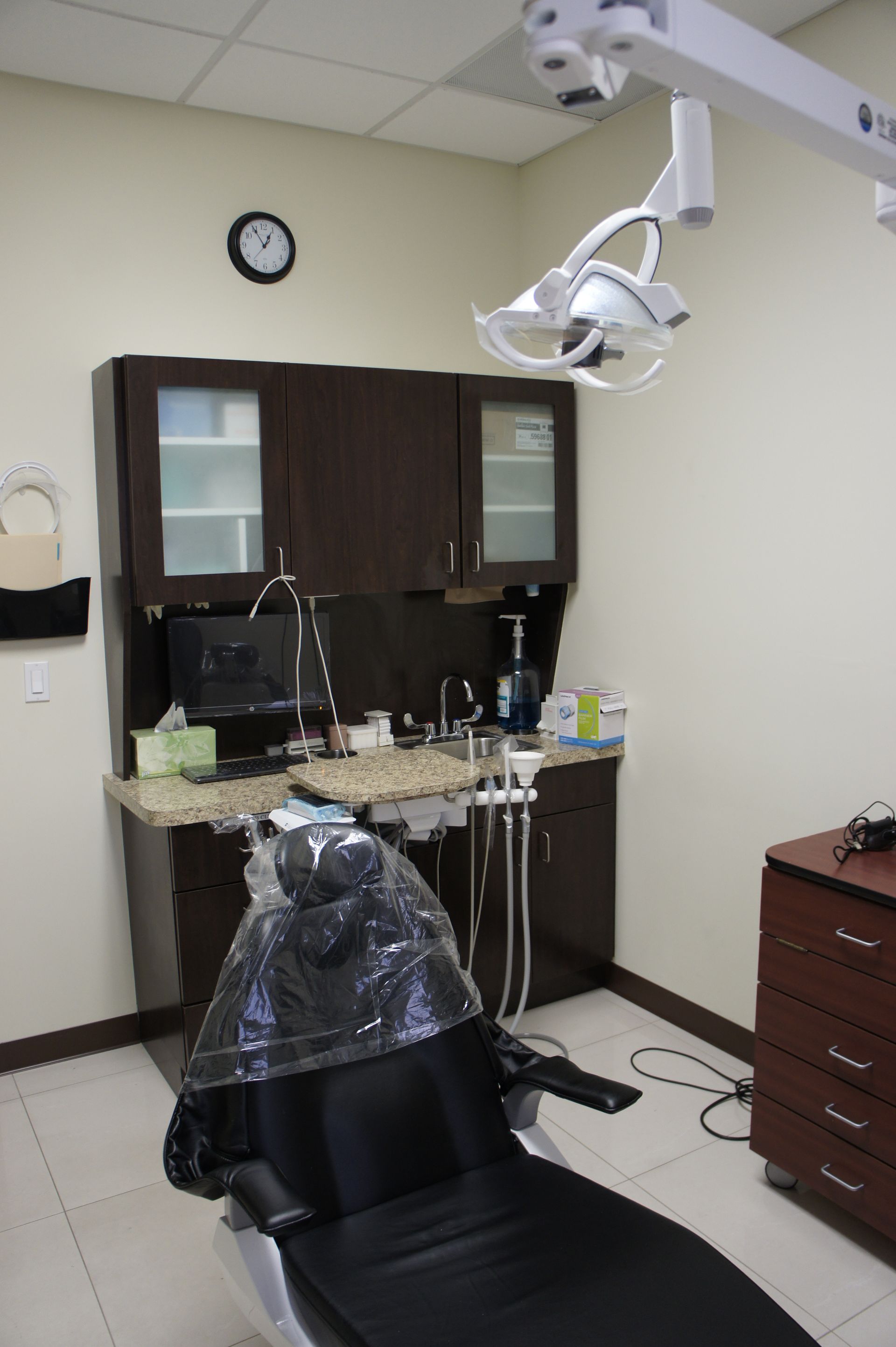 Dental office interior with chair, cabinets, light, sink, and clock.