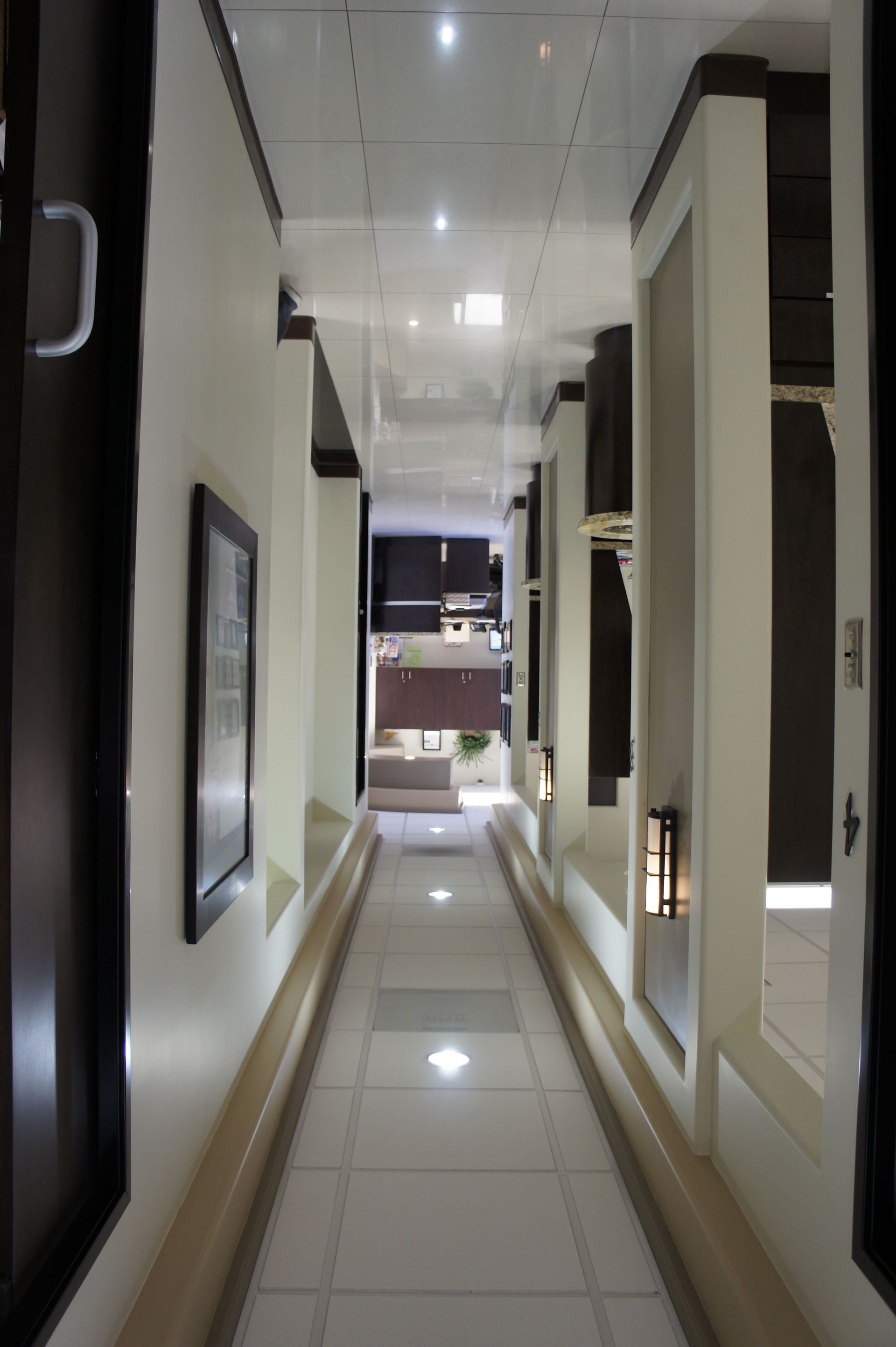 Narrow hallway with white tile floor, framed artwork, and recessed lighting.