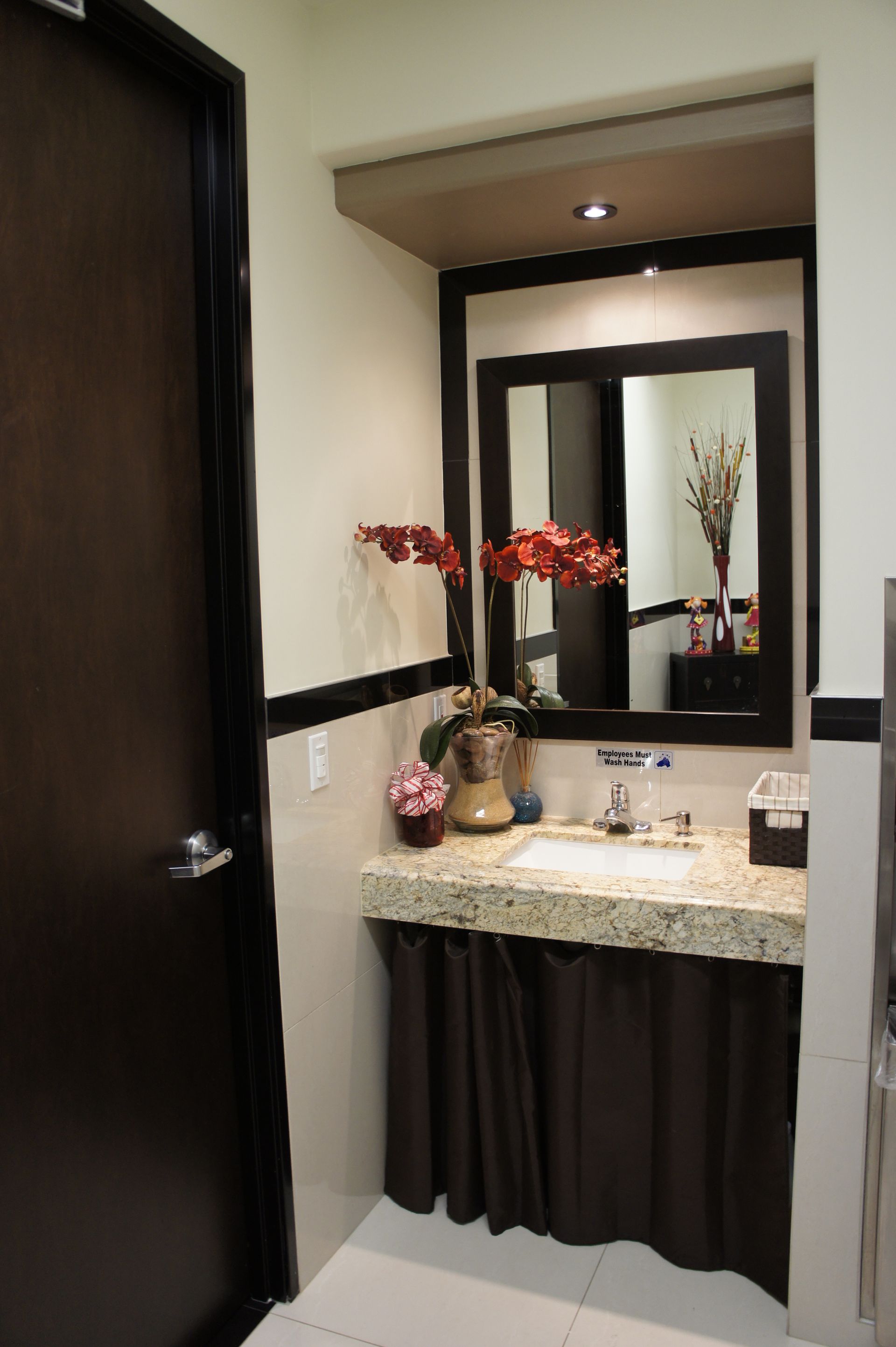 Dark-trimmed bathroom with a granite countertop vanity, large mirror, and dark door.
