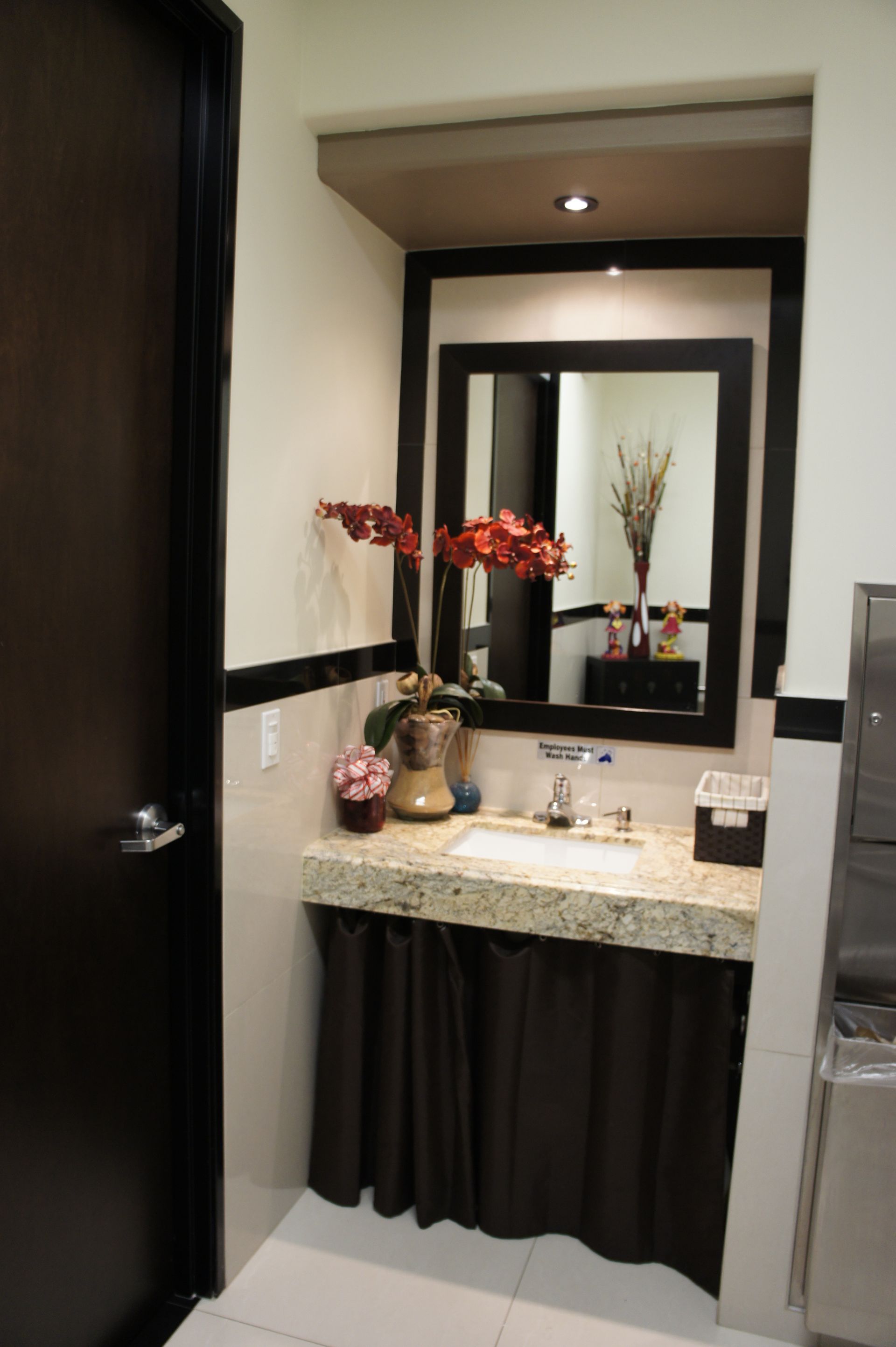 Bathroom with sink, mirror, and decor. Dark brown door and vanity skirt. White, beige, and brown colors.