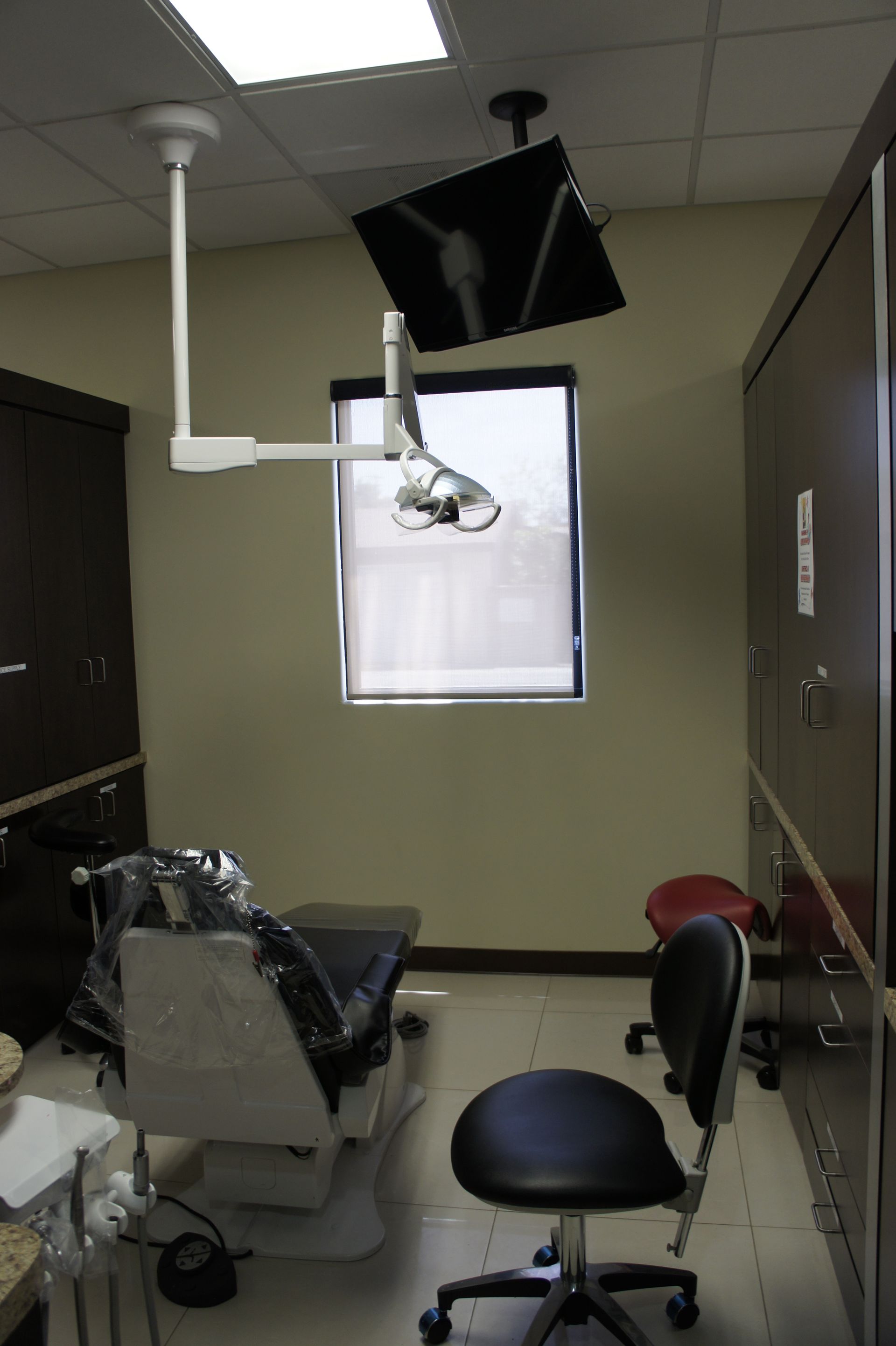 Dental office with a patient chair, black equipment, window, and cabinet.