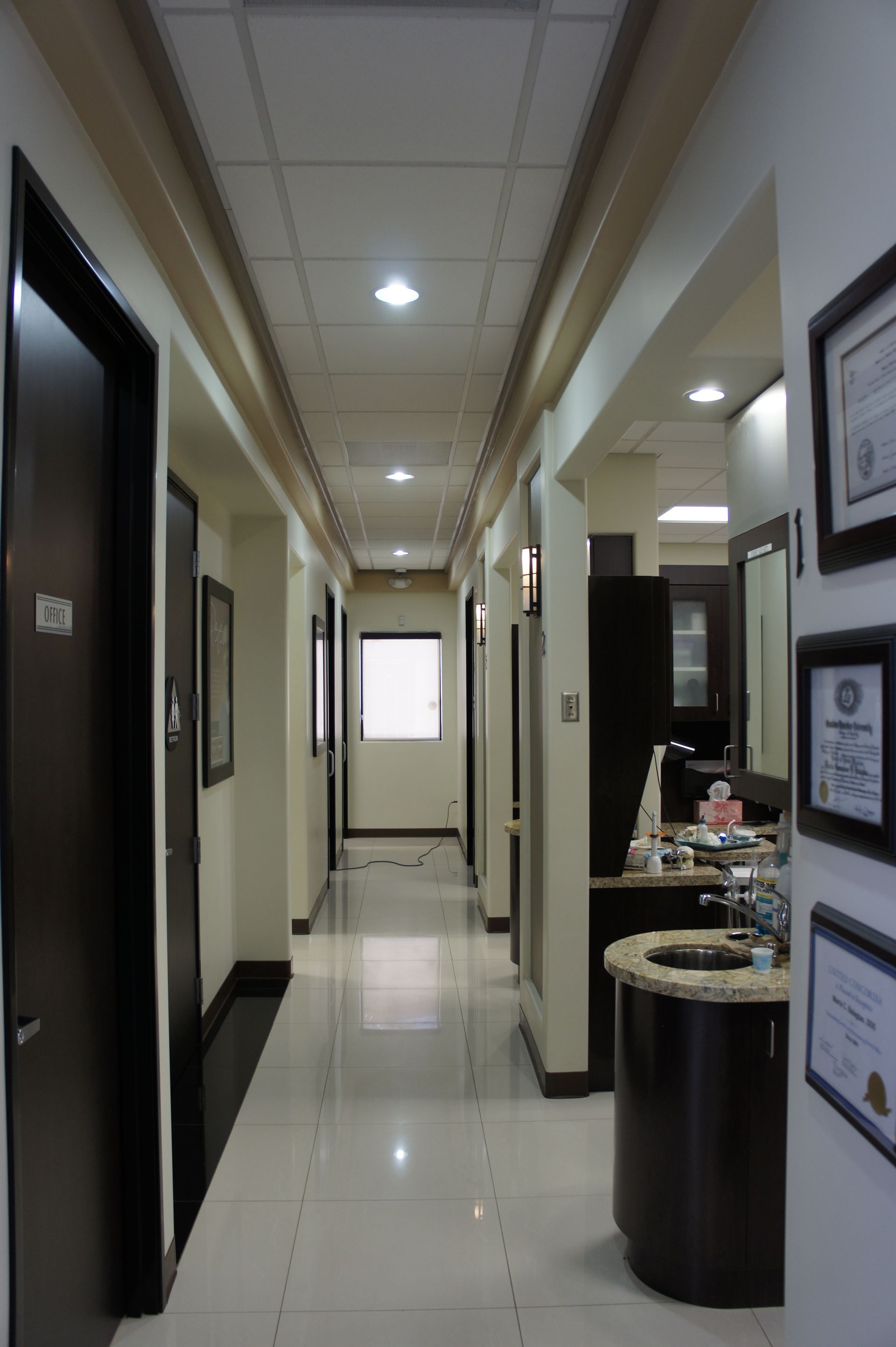 Hallway with doors, recessed lighting, and framed certificates on the wall.