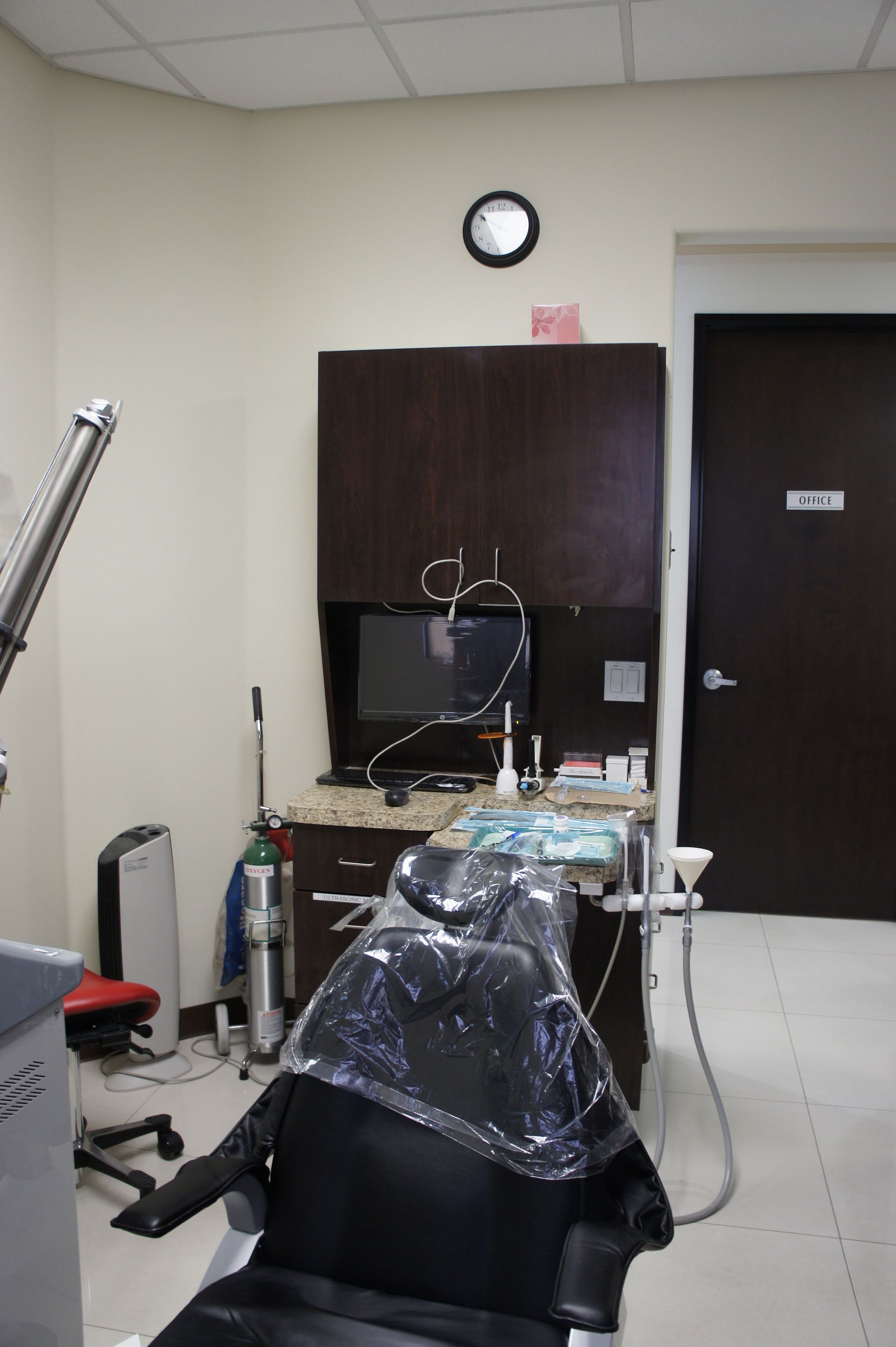 Dental office interior: dental chair, dark cabinets, equipment, door, and clock.