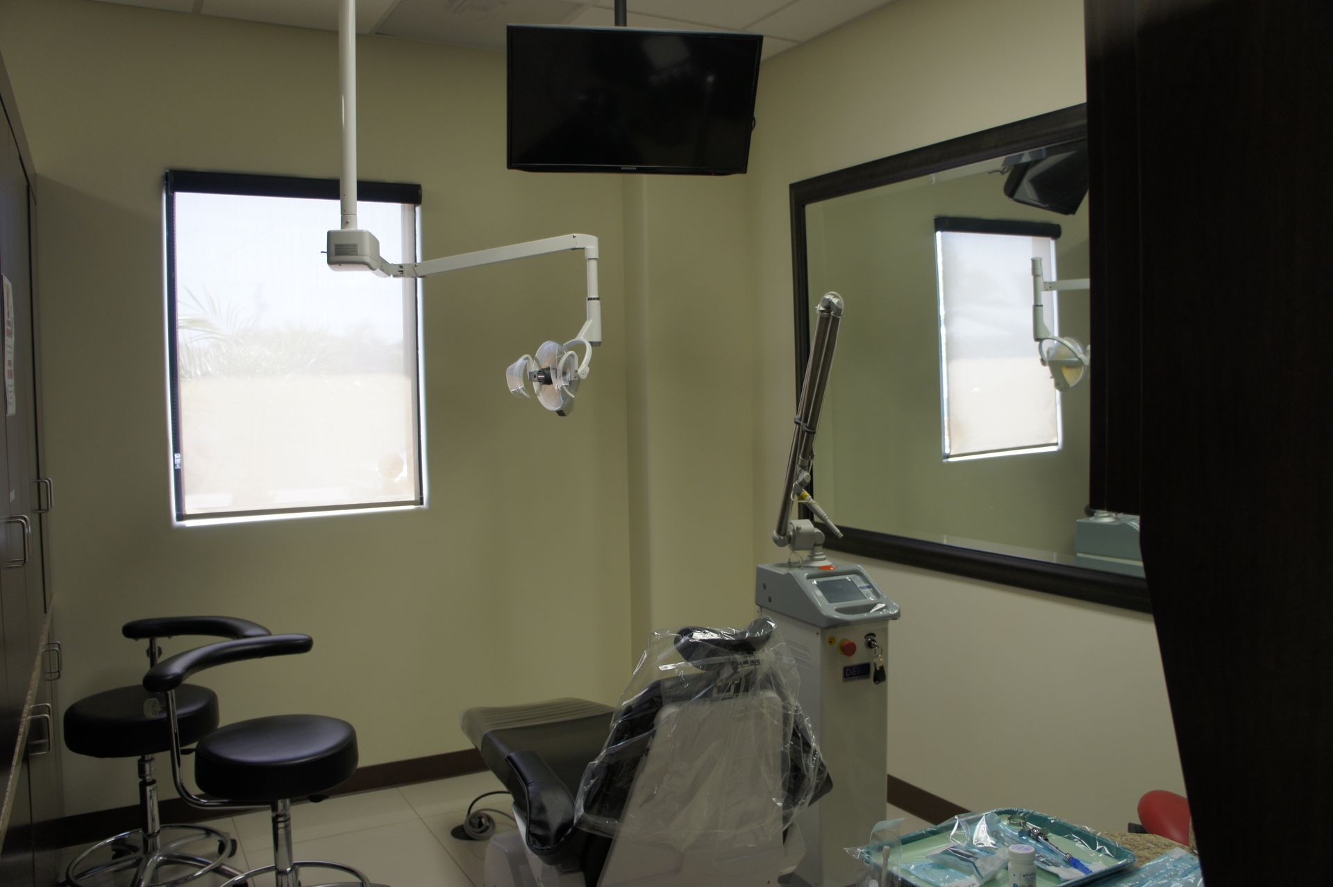 A dentist's office with a dental chair, a TV, a mirror, and medical equipment.