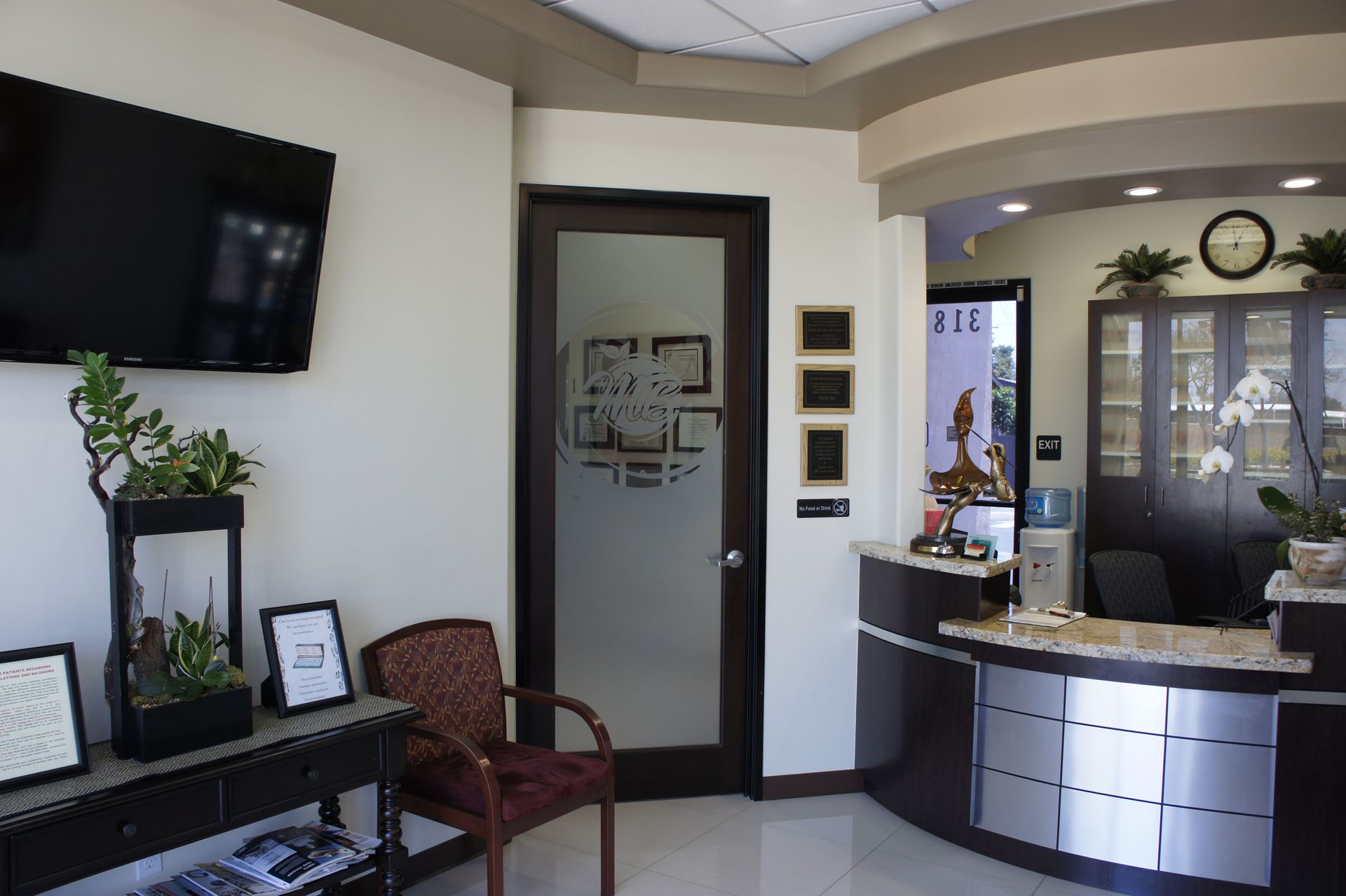 A modern dentist office waiting area with a reception desk, plants, and a TV.
