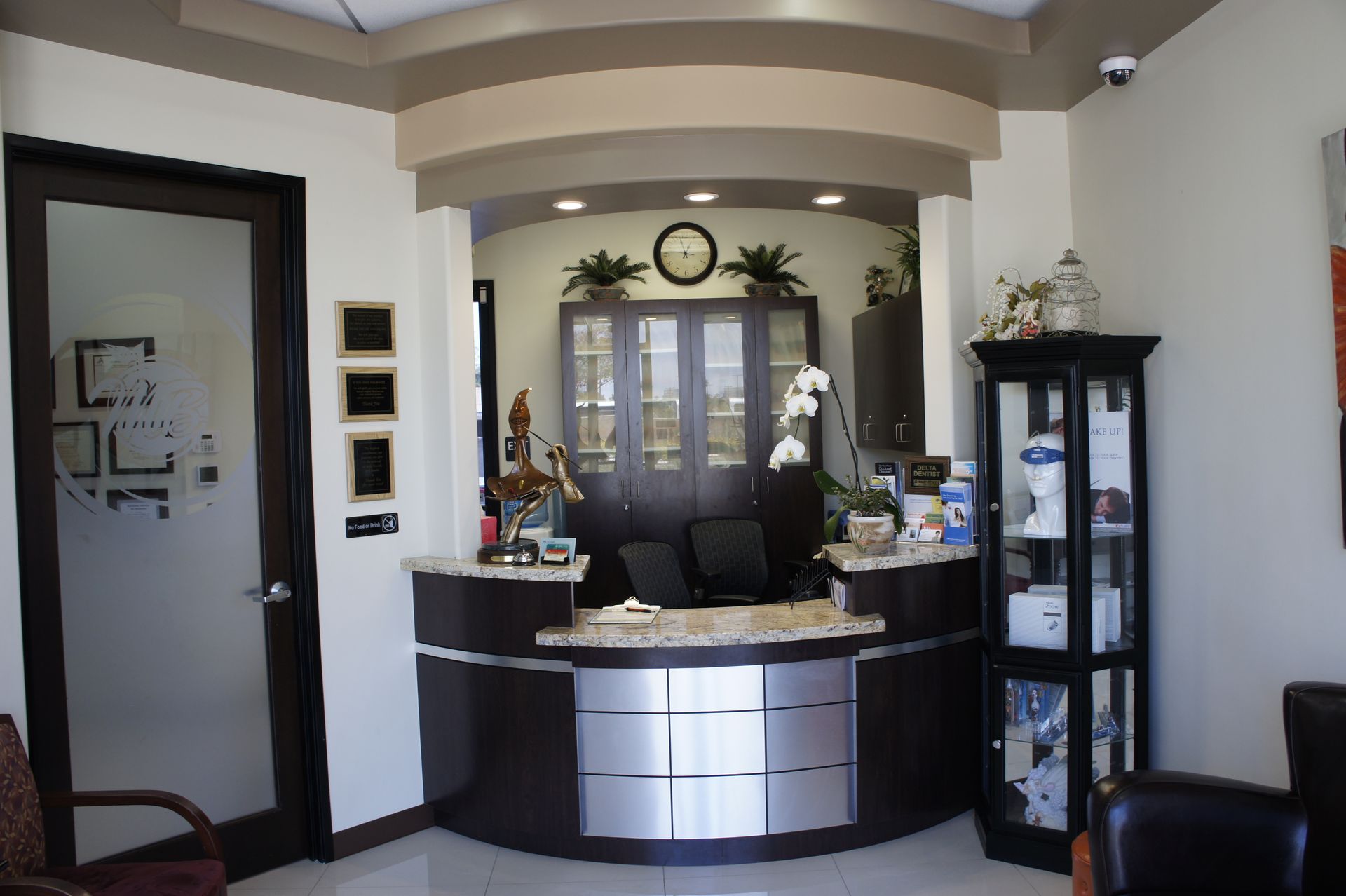 Reception area with a curved front desk. Brown and silver tones, with waiting chairs.