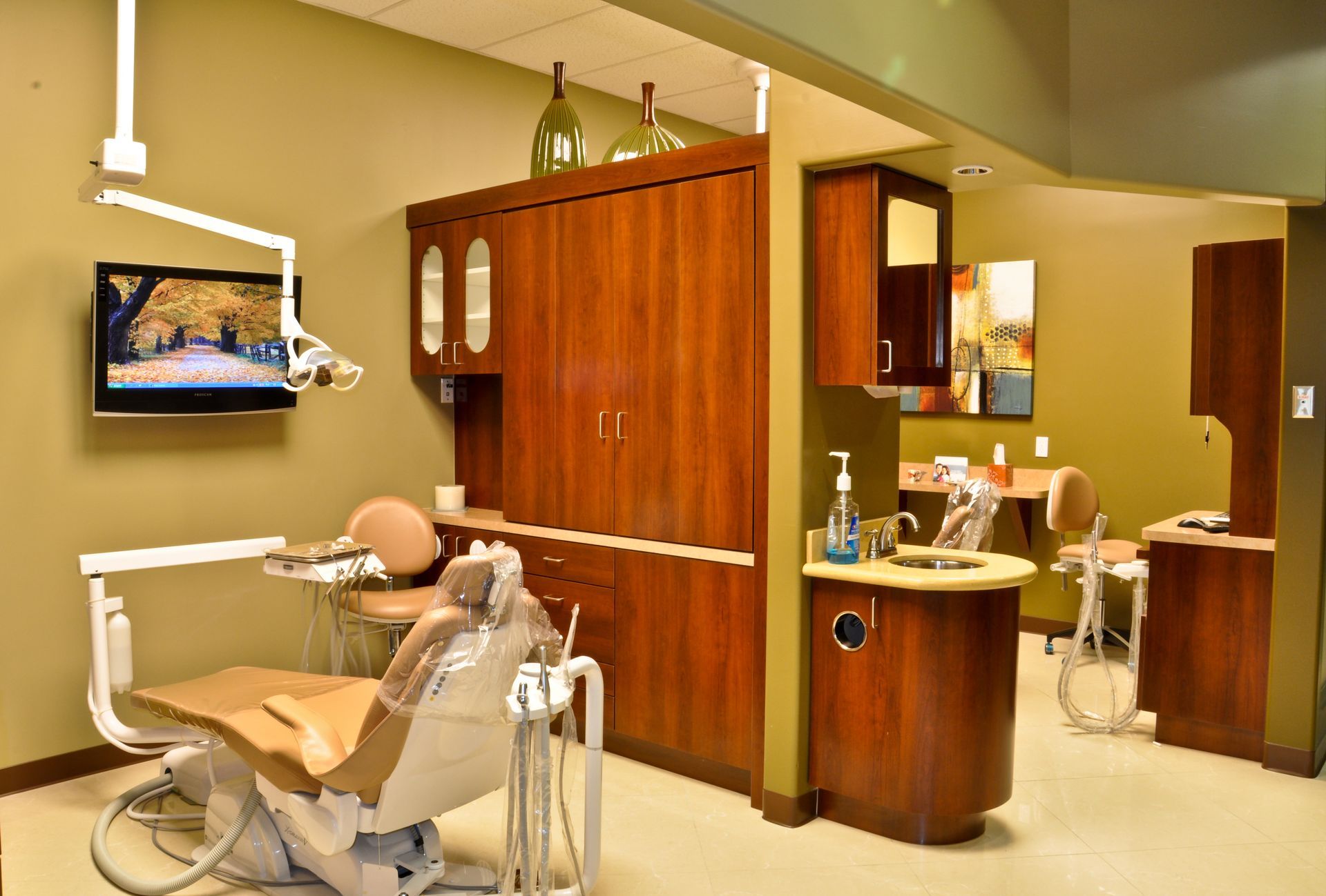 Dental operatory with a chair, cabinets, tools, and a monitor showing a fall scene.